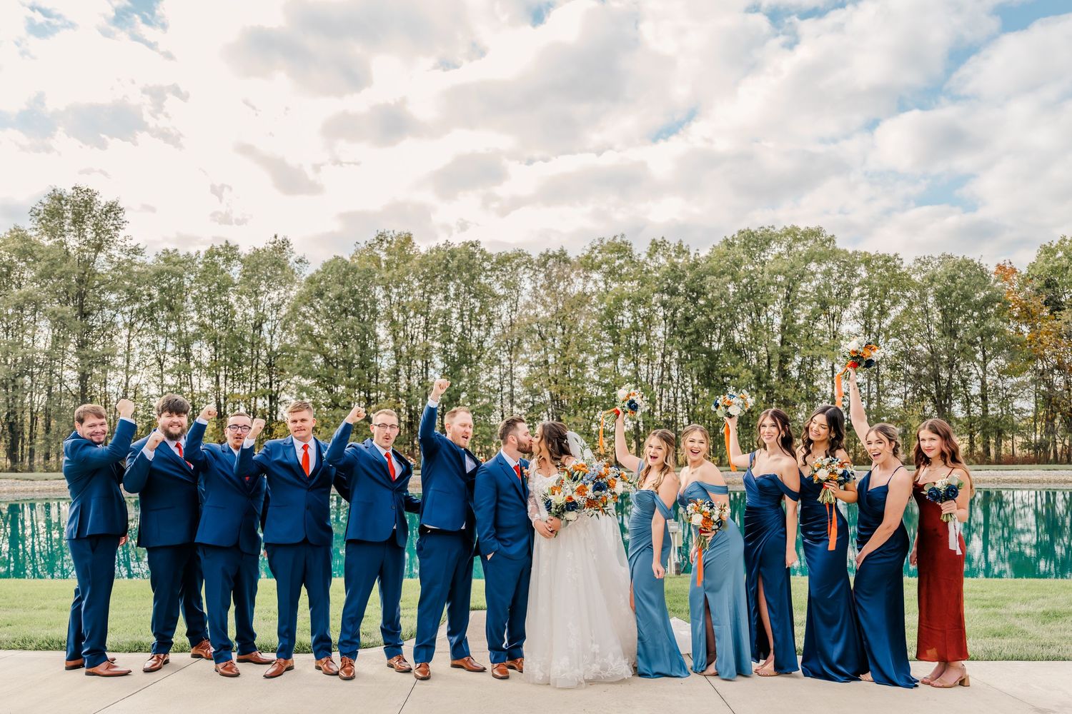 Wedding party in navy and light blue attire poses together in front of autumn trees. Four Seasons Barn Wedding & Event Venue