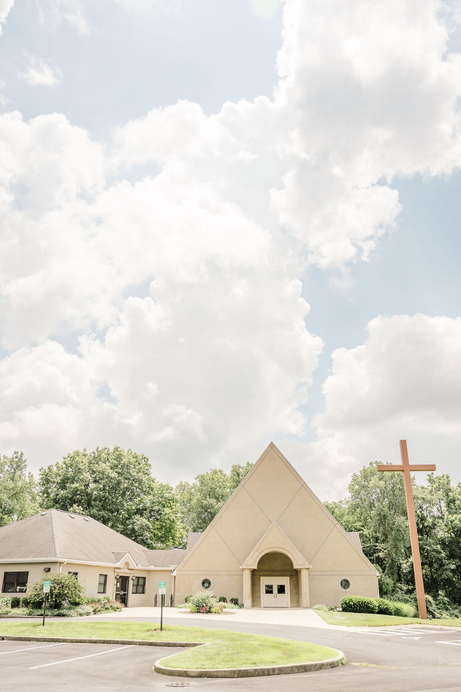 Modern church building exterior with pyramid-shaped architecture and cross under cloudy skies.