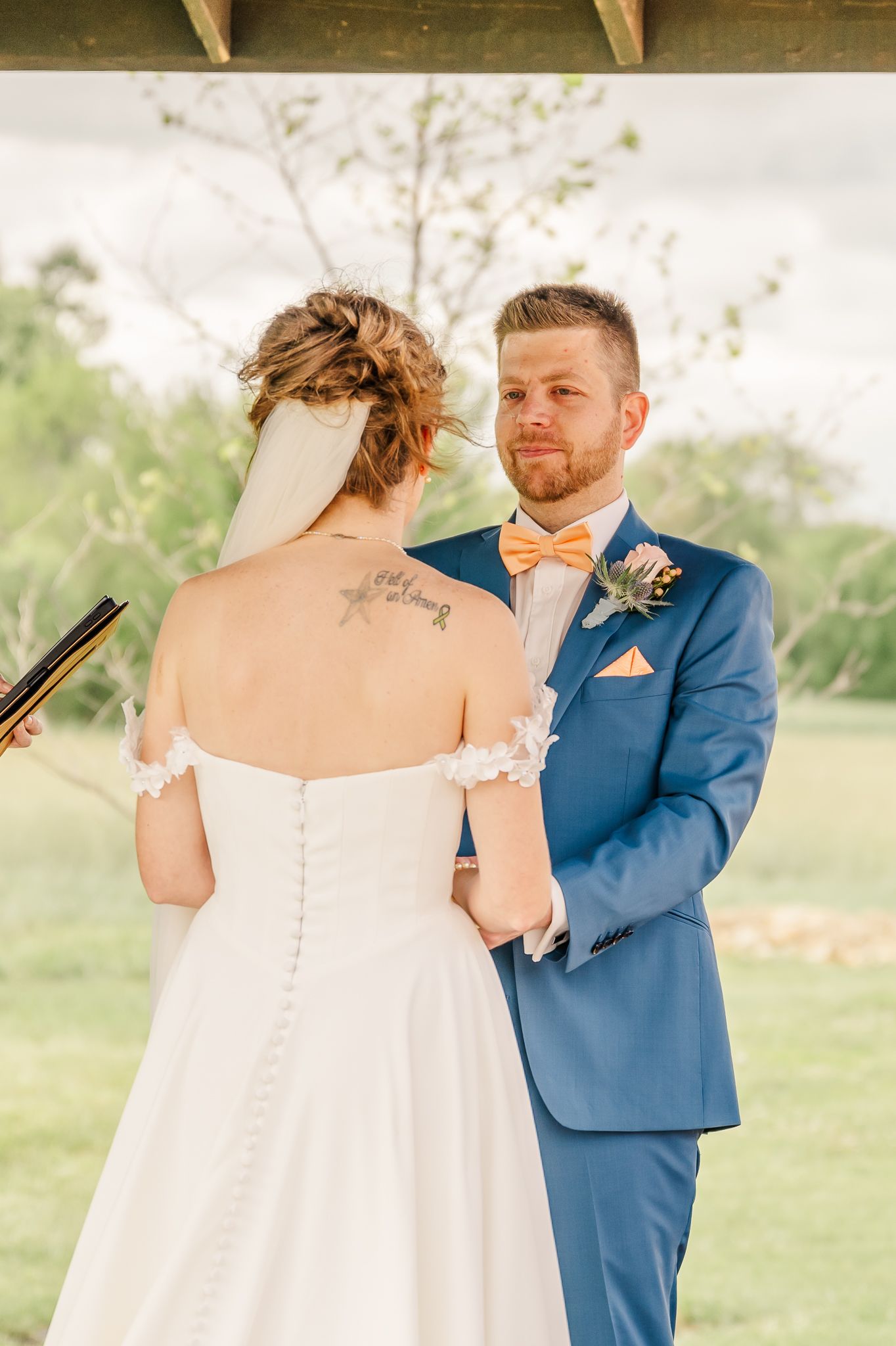 Groom in blue suit with peach bow tie holds bride's hands during outdoor wedding ceremony.The Old Barns at Dry Run Farms in Williamsport, Oh