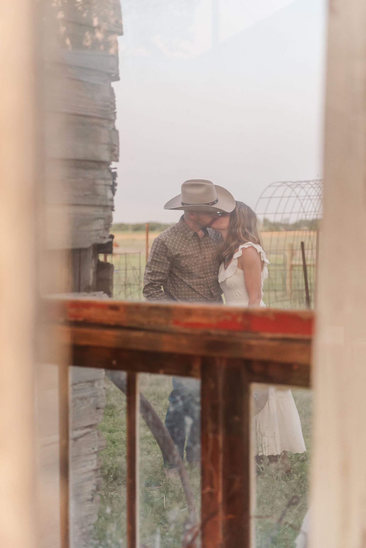 A dreamy rustic scene photographed through a window frame showing a couple sharing an intimate moment on a farm.