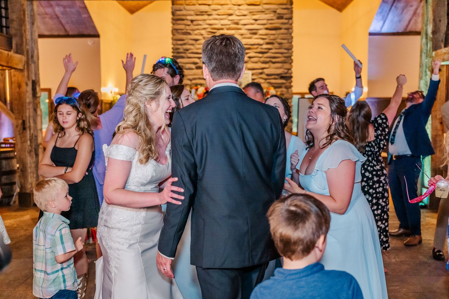 Guests dancing and celebrating on a wooden dance floor at an indoor wedding reception.