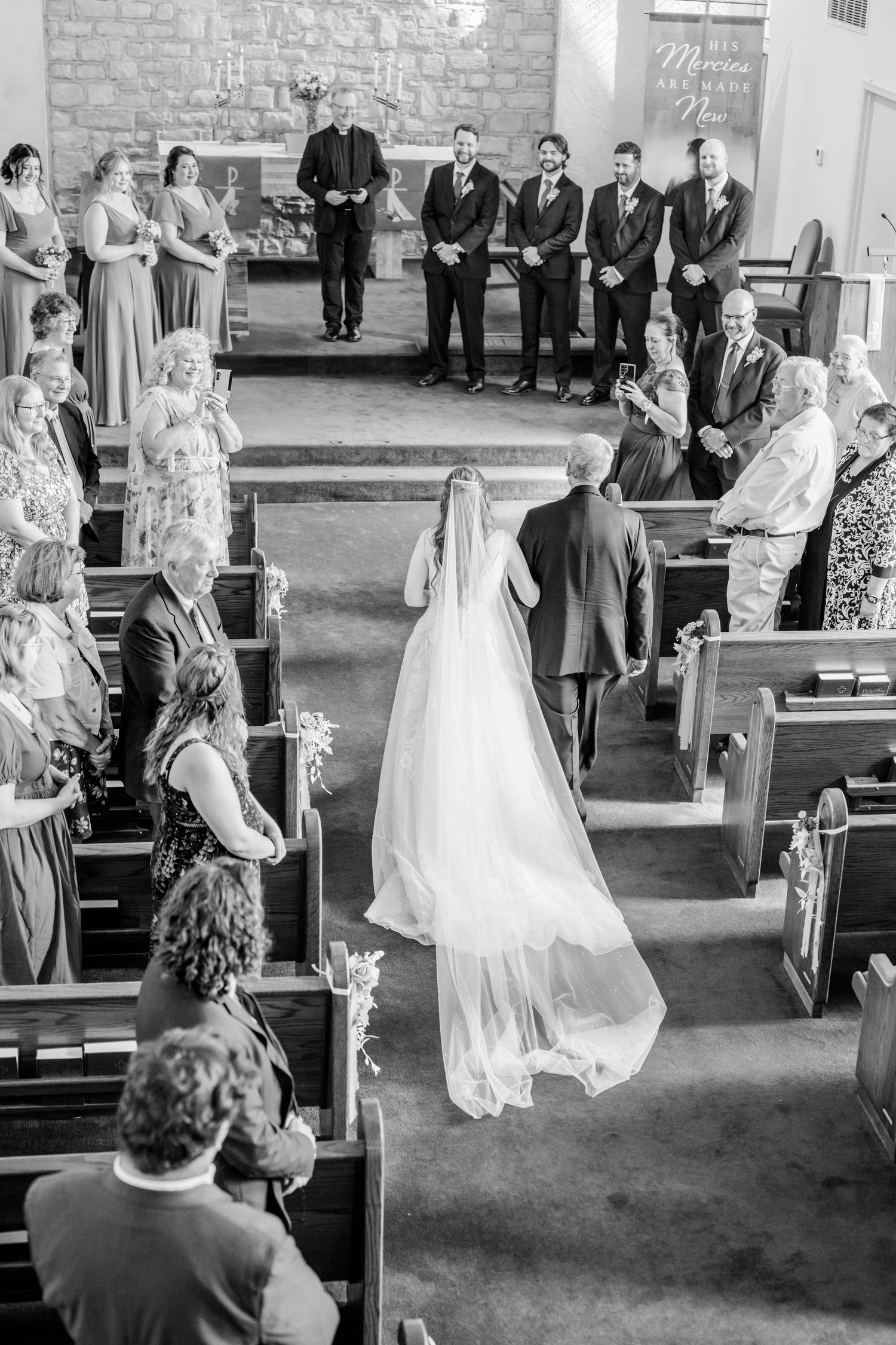 Black and white photo of wedding ceremony in traditional church with guests in pews.