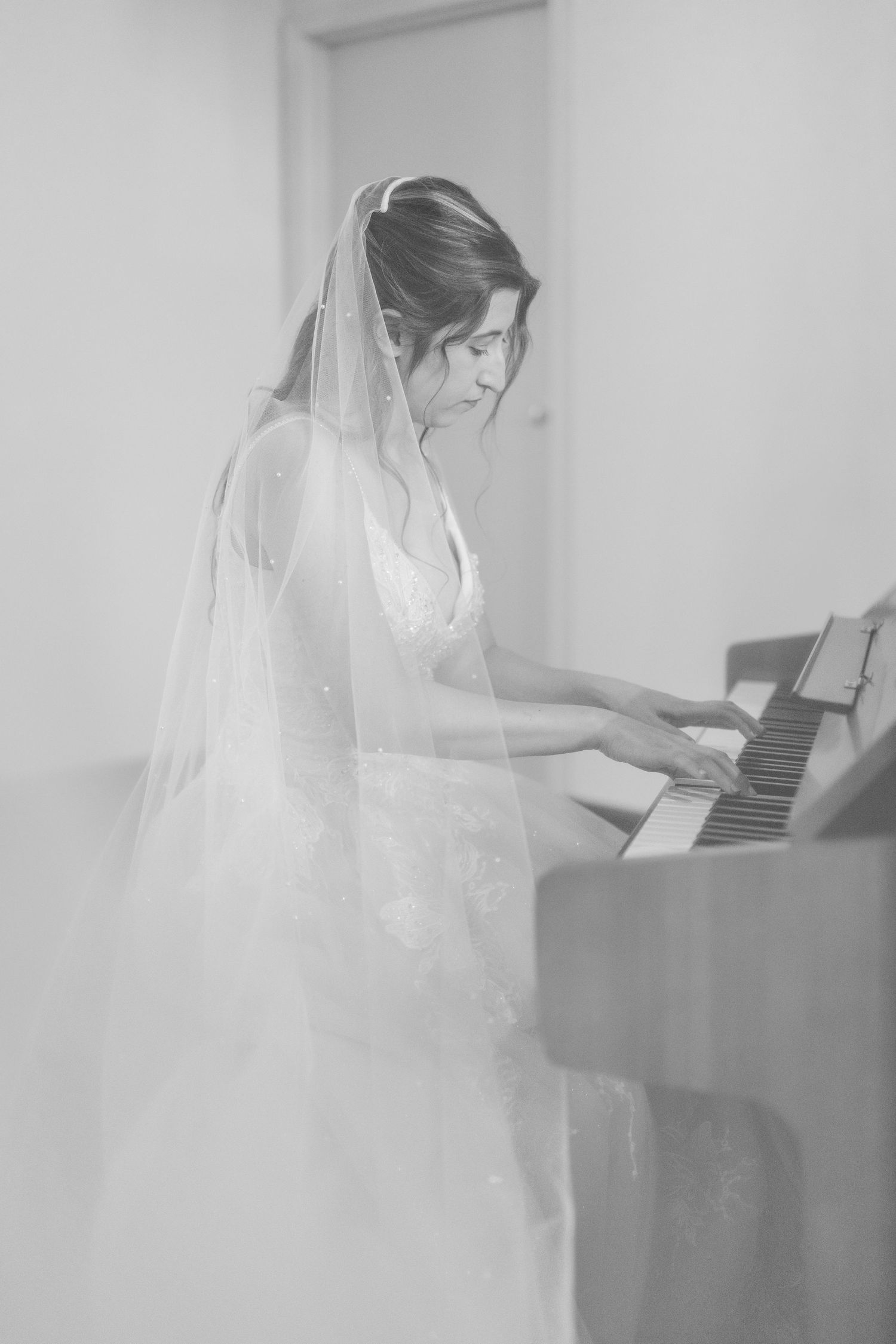 Ethereal black and white photo of bride in veil playing piano.