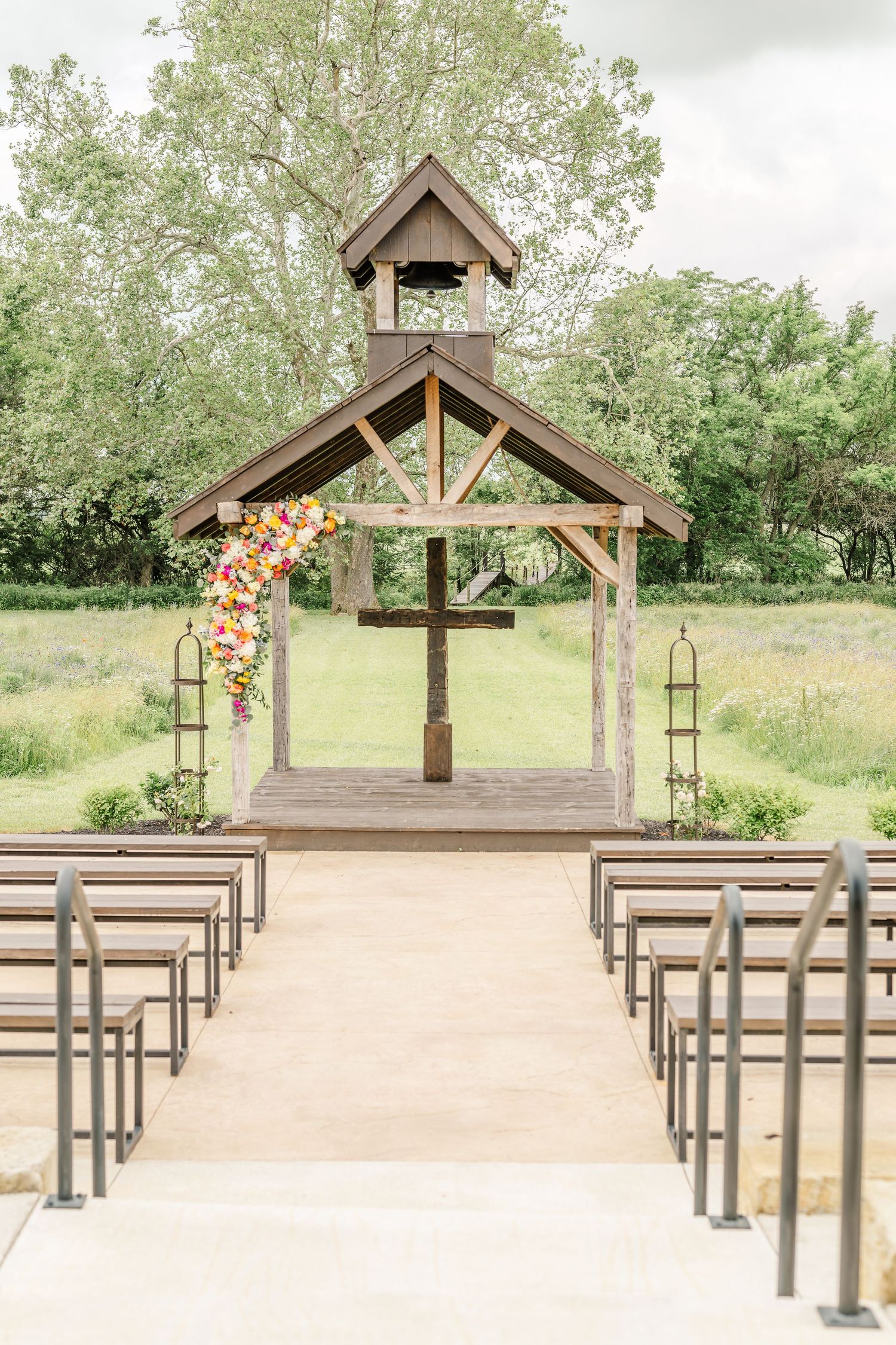 Rustic outdoor wedding chapel with wooden benches & floral arch decorations in a natural setting. The Old Barns at Dry Run Farms in Williams