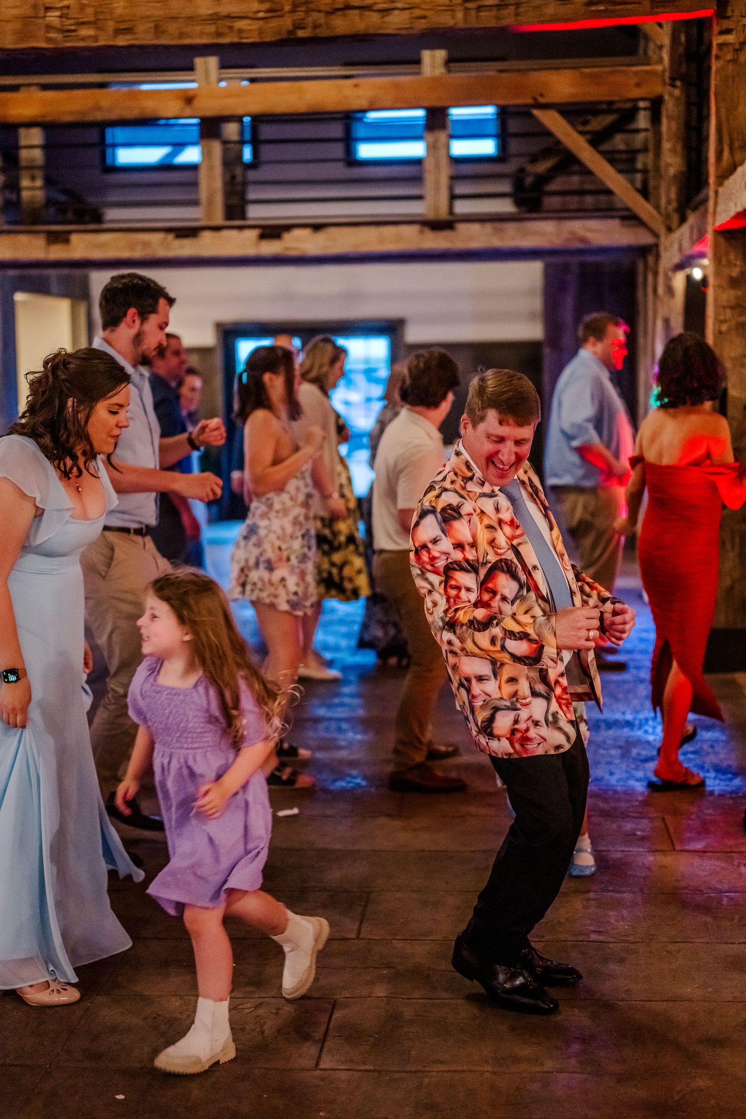 People dancing and having fun at a rustic indoor venue with wooden beams and colorful lighting during a celebration.