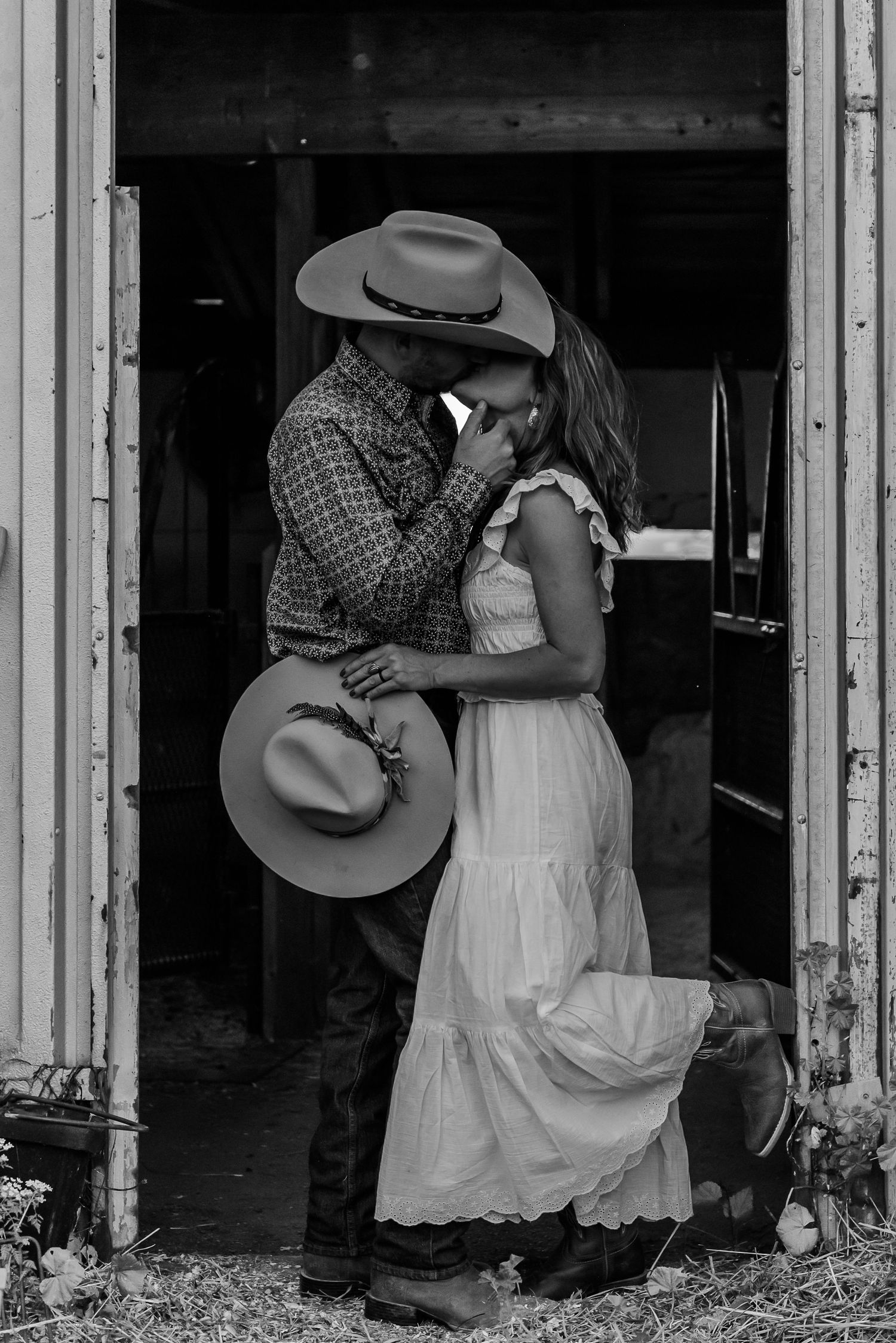 Romantic couple embracing in rustic barn doorway wearing country western attire.