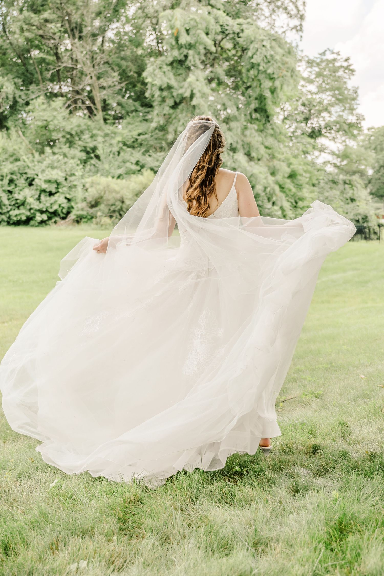 A flowing white wedding dress billows gracefully in the breeze as someone twirls on green grass in a garden setting.