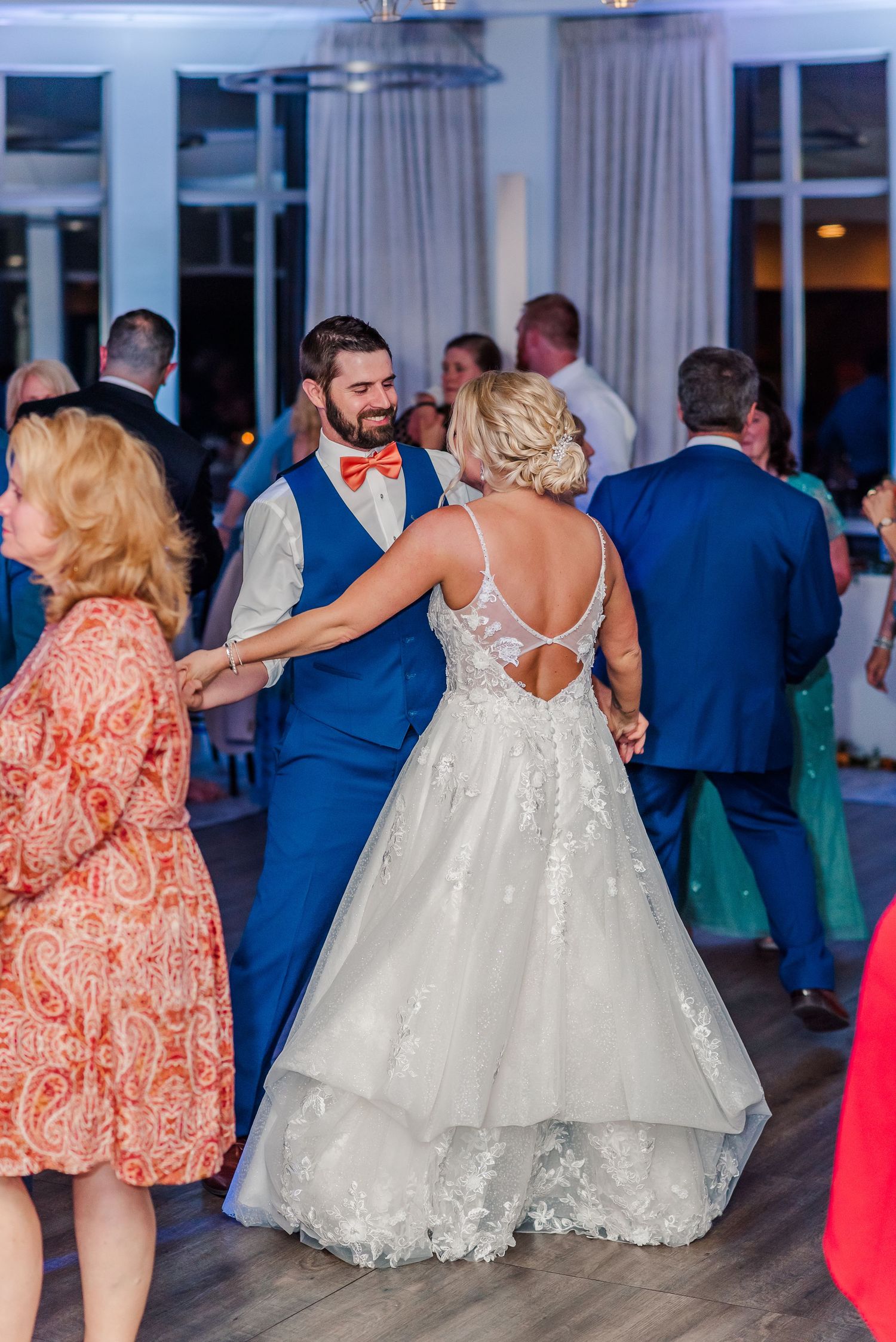 Guests dancing at a wedding reception with the bride in a beautiful lace gown and groom in a blue suit.