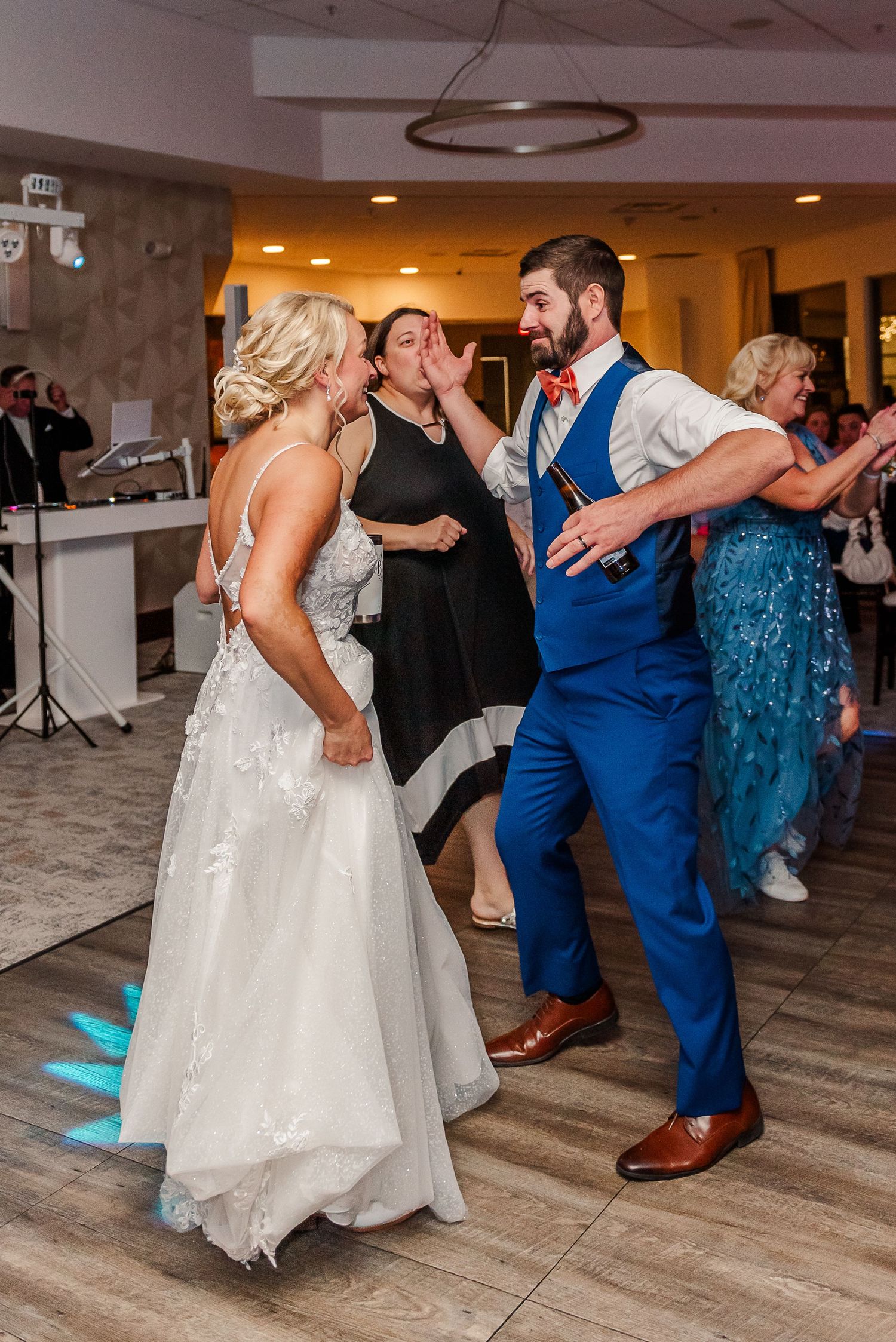 Wedding couple performs a playful dip dance move sequence on a light wooden floor with guests in the background.