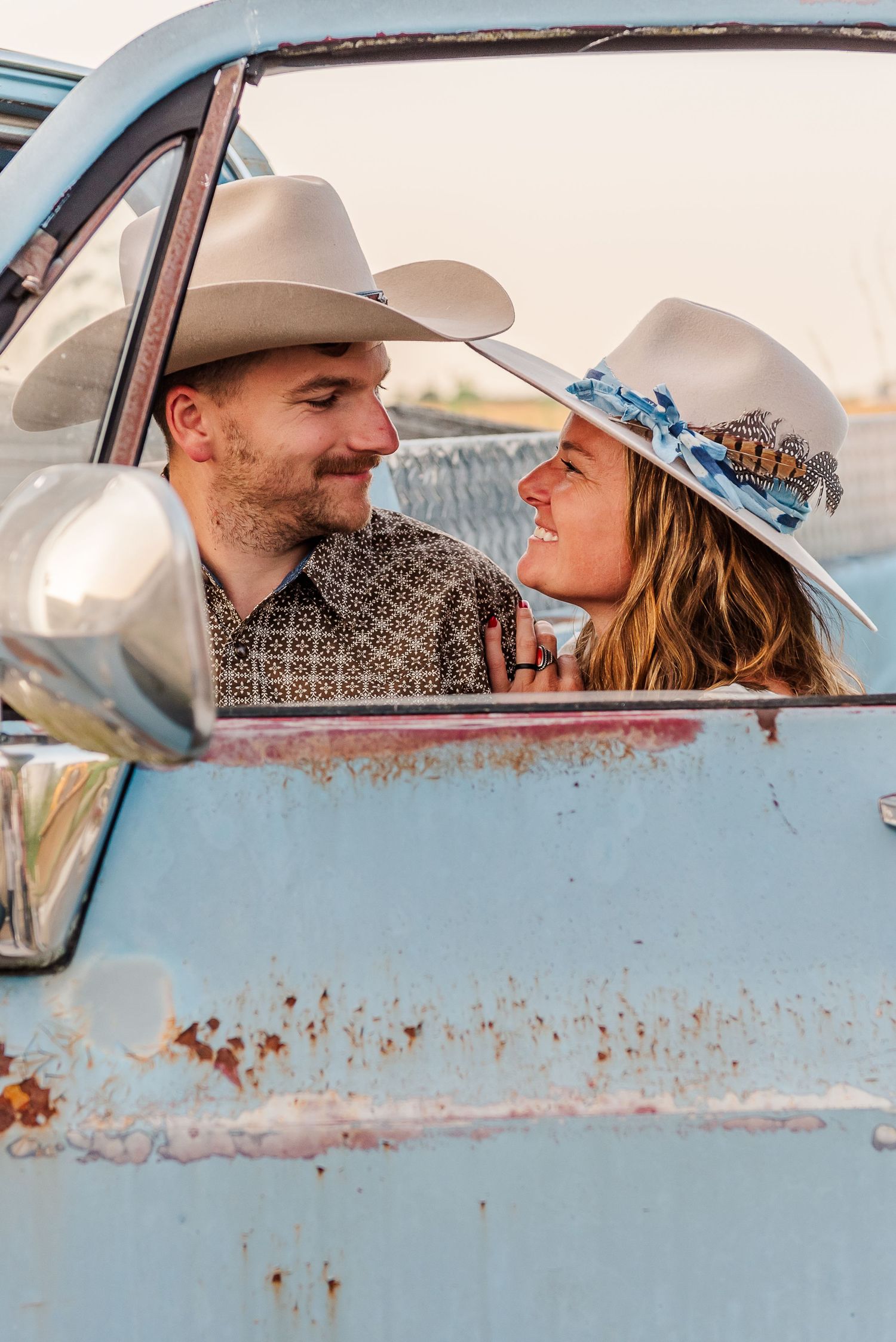 A romantic couple shares tender moments in a vintage blue car during a sunset photoshoot.