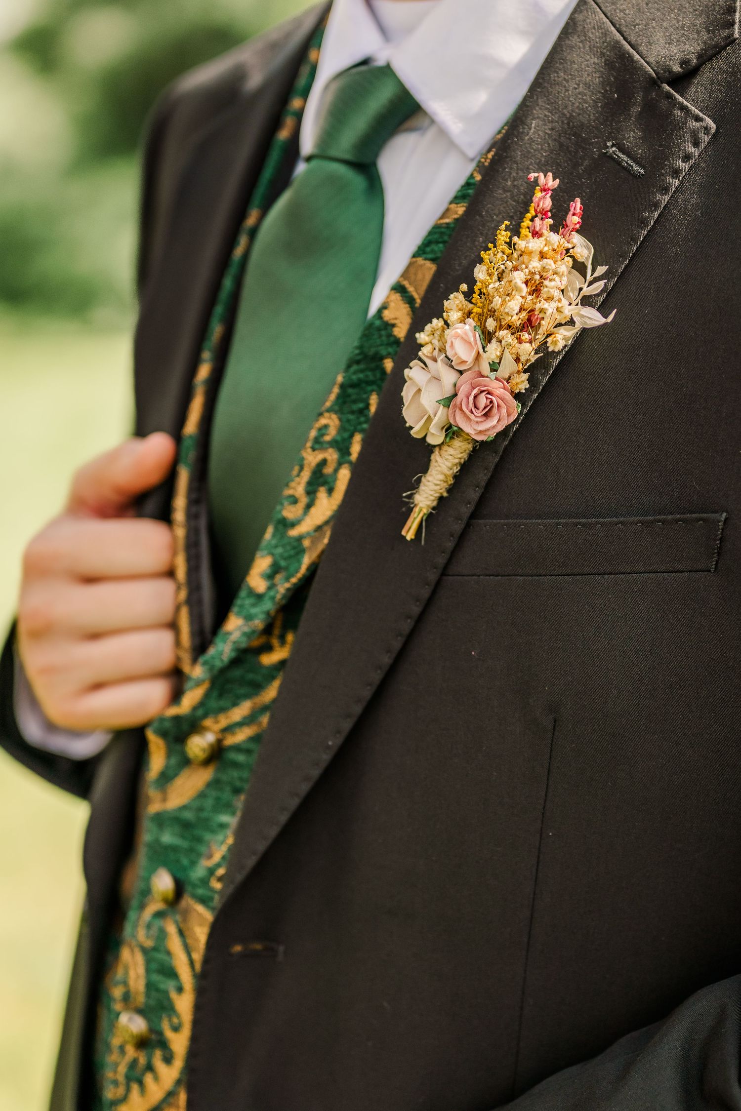 Close-up of groom's boutonniere with dried flowers on dark suit jacket with emerald green tie.