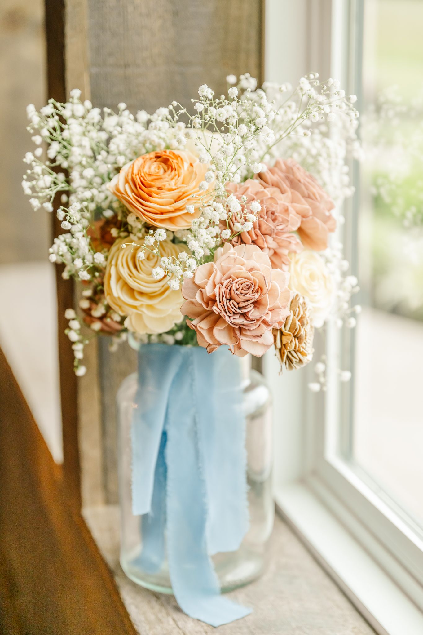 Elegant bridal bouquet of peach roses and baby's breath in a glass vase tied with a light blue ribbon. The Old Barns at Dry Run Farms