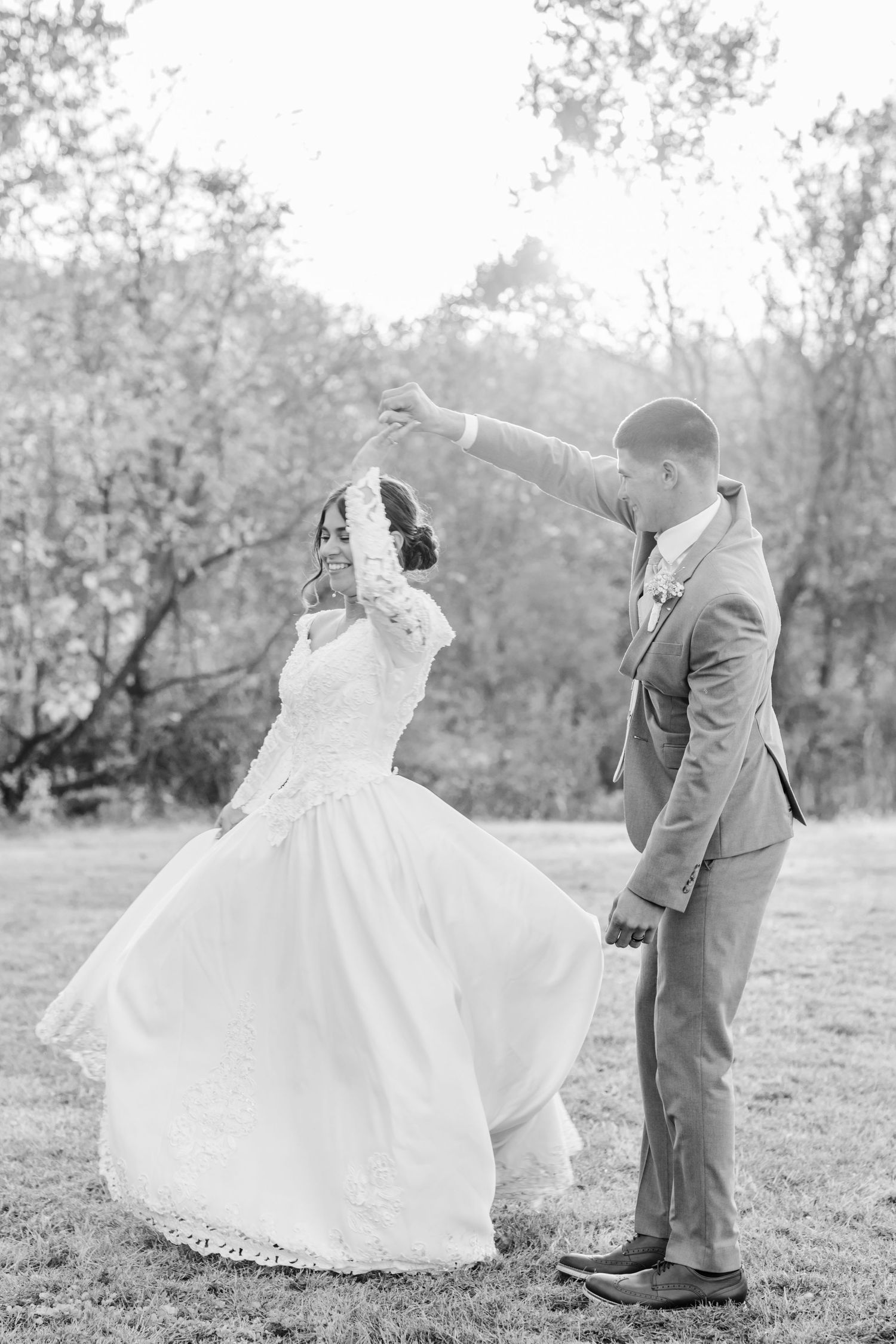 A romantic wedding couple dances and twirls in a sunlit outdoor field wearing gray suit and white ballgown dress. Fall wedding photography.