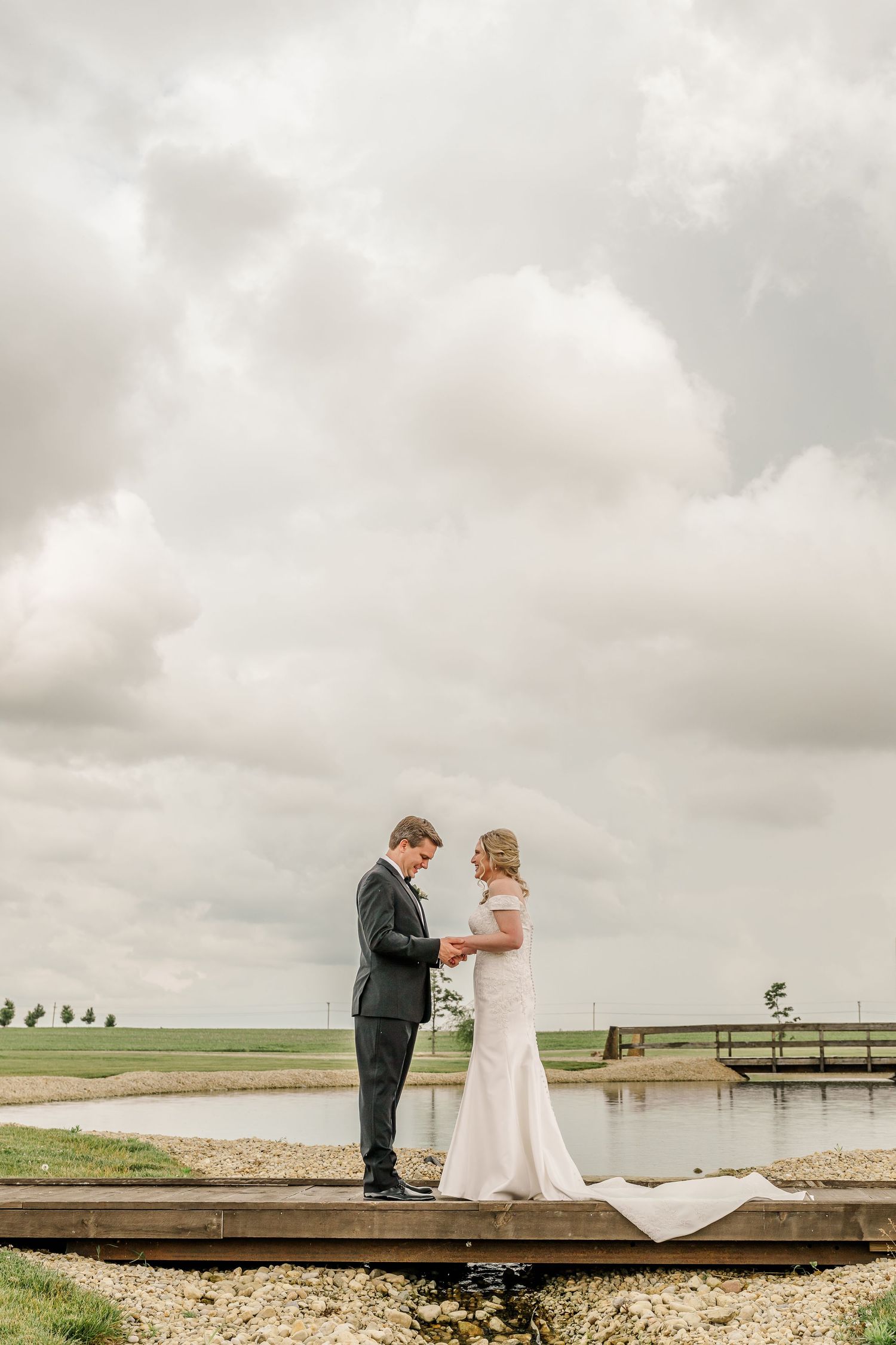 A couple stands on a wooden deck overlooking a serene lake under cloudy skies. The Old Barns at Dry Run Farms in Williamsport, OH.