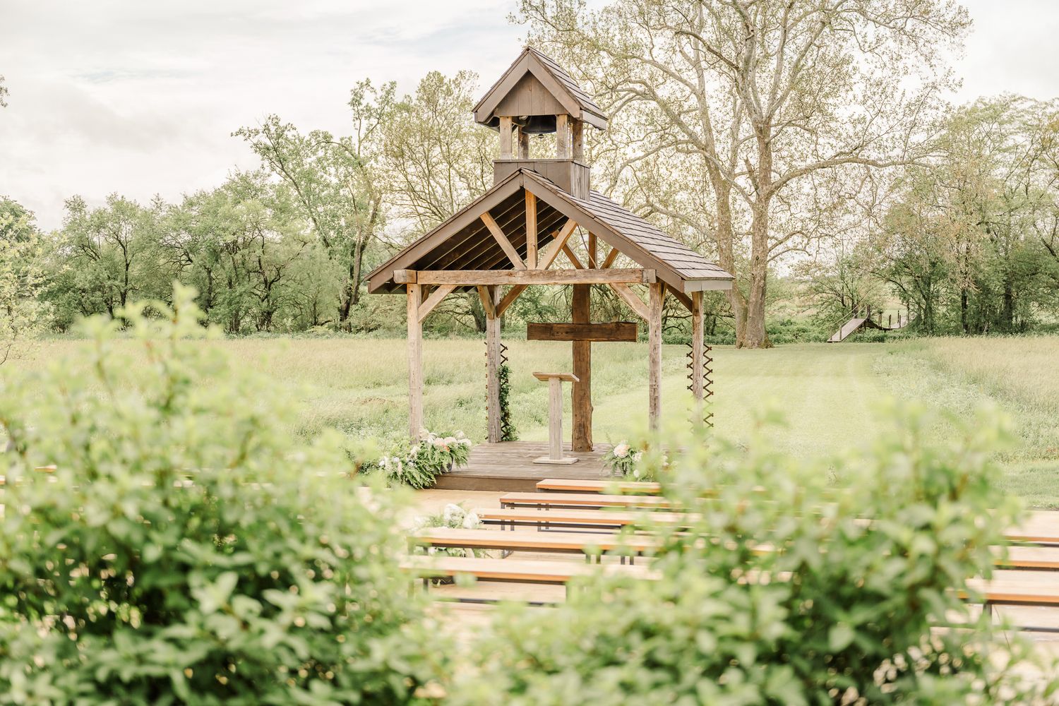 Rustic wooden chapel with cross and benches in a lush green meadow, perfect for outdoor wedding ceremonies.The Old Barns at Dry Run Farms