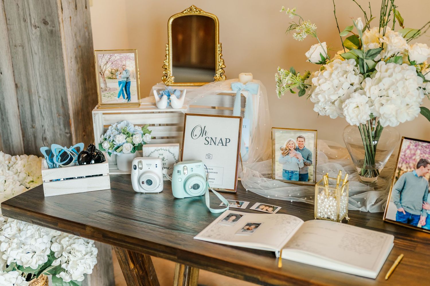 Elegant wedding reception table setup with white floral arrangements, rustic decor, and vintage-inspired signage.