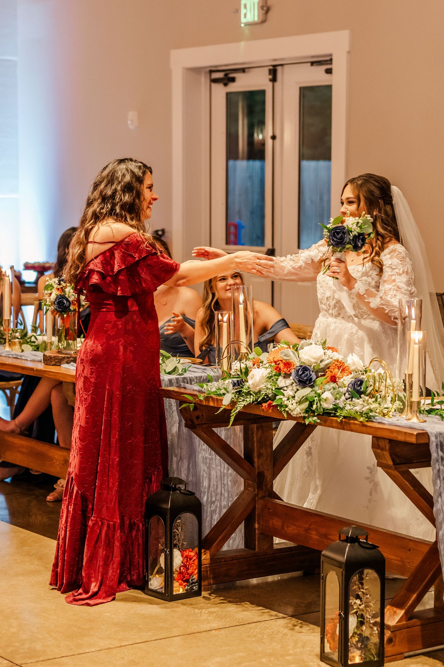 Wedding party seated at an elegant reception table with burgundy dresses and floral centerpieces.