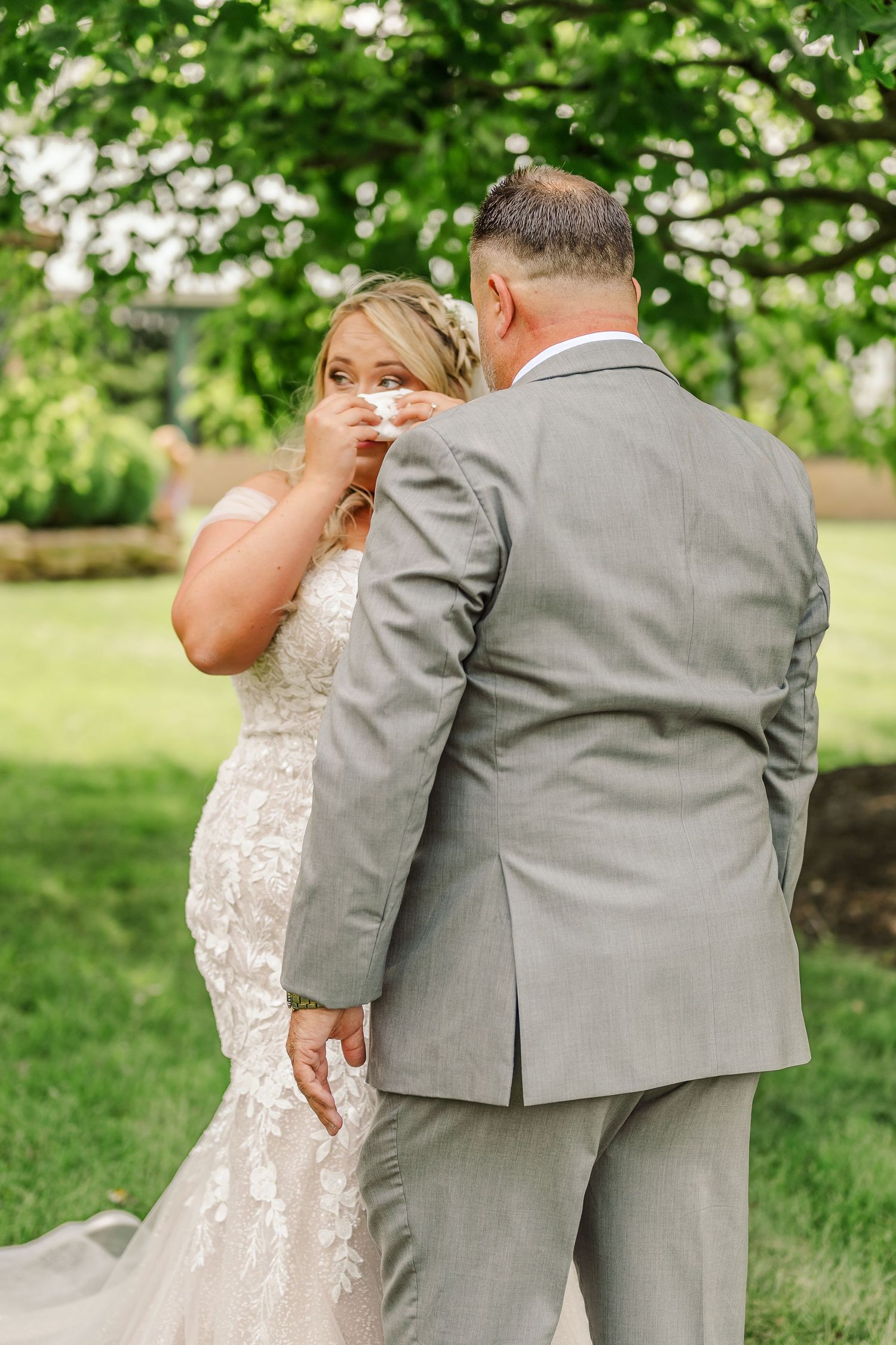 A couple shares a tender moment outdoors surrounded by lush green trees and foliage.