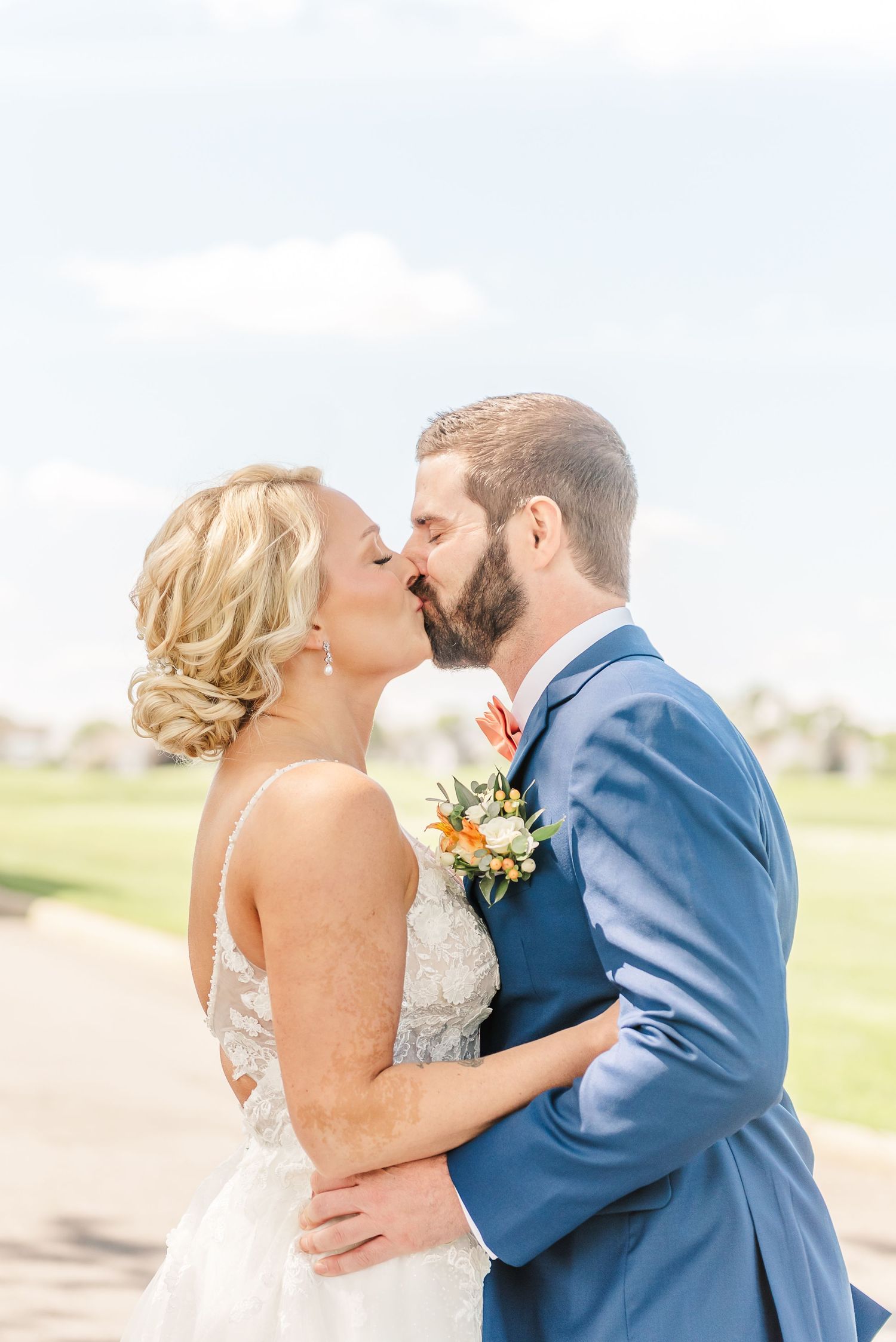 Romantic newlywed couple sharing their first kiss as husband and wife at an outdoor wedding venue.