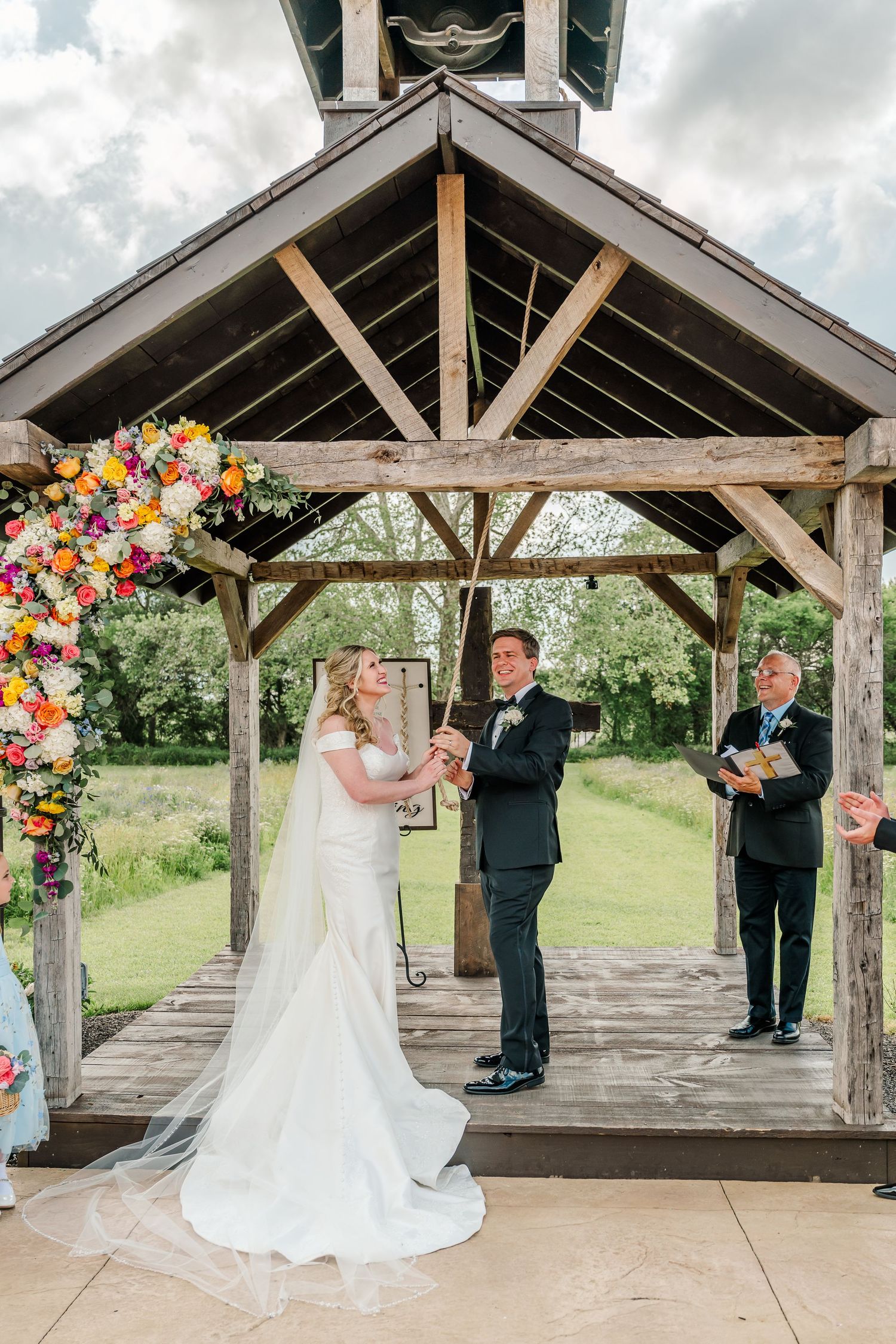 Wedding ceremony takes place under a rustic wooden pavilion decorated with vibrant floral arrangements.The Old Barns at Dry Run Farms