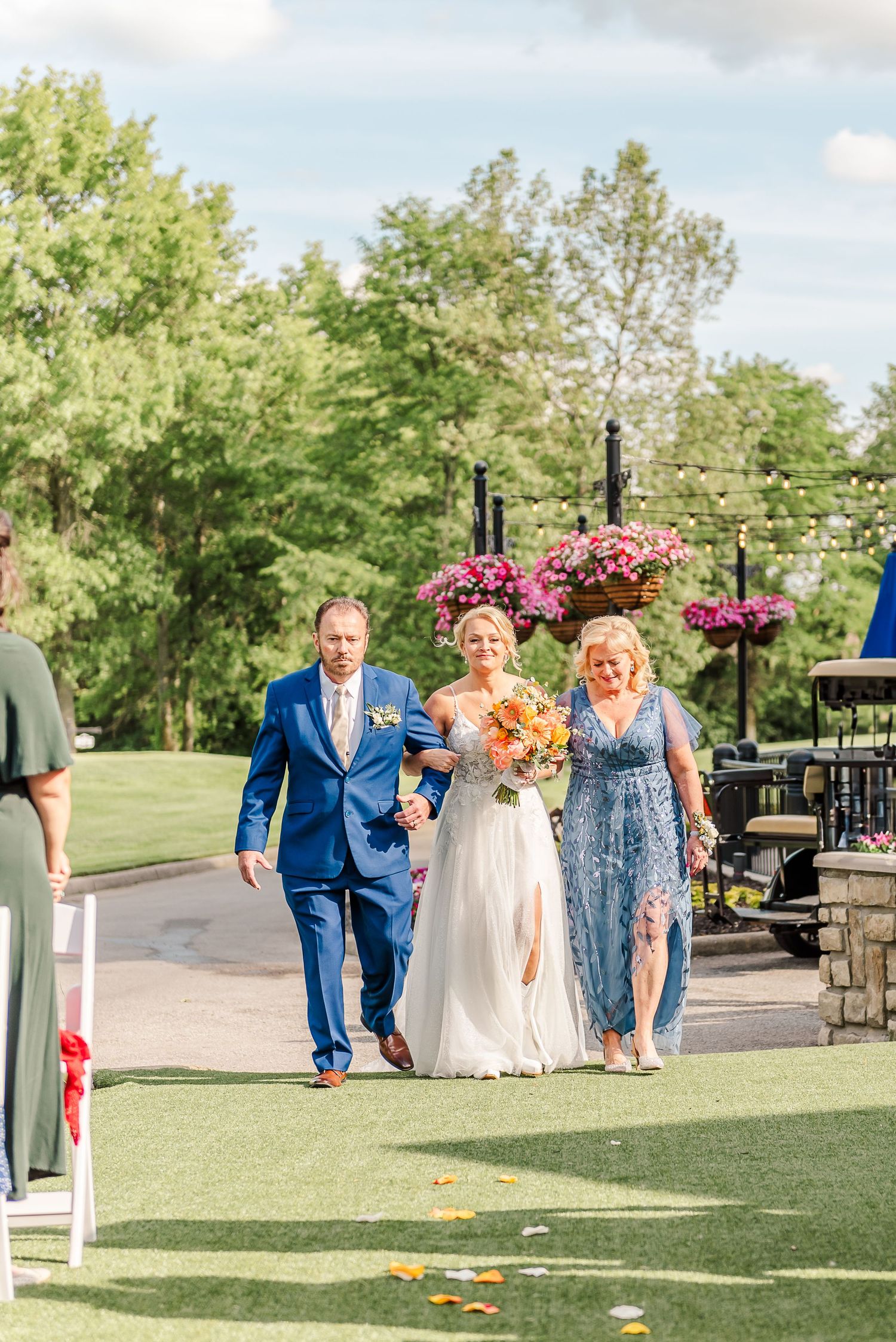 Wedding processional on an outdoor path with guests watching the ceremony entrance.