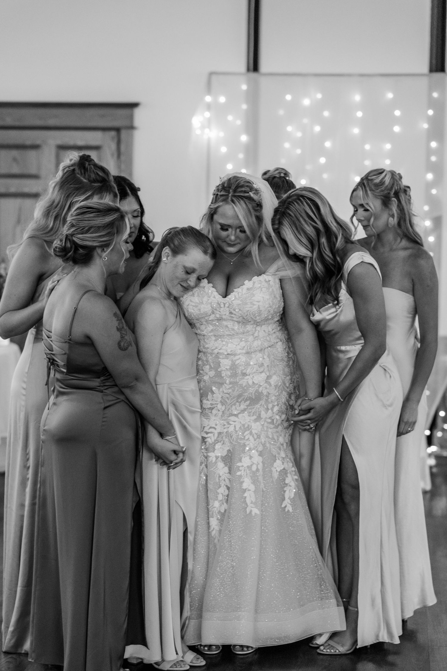 A touching moment as bridesmaids in elegant gowns gather around to admire a wedding dress.