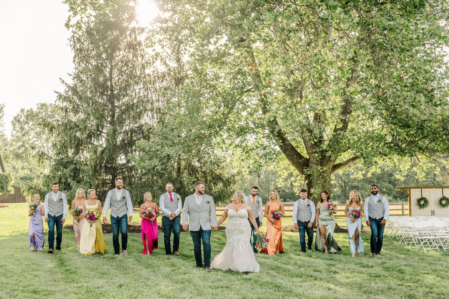 Wedding party members lined up on a grassy lawn with trees in the background during an outdoor celebration.