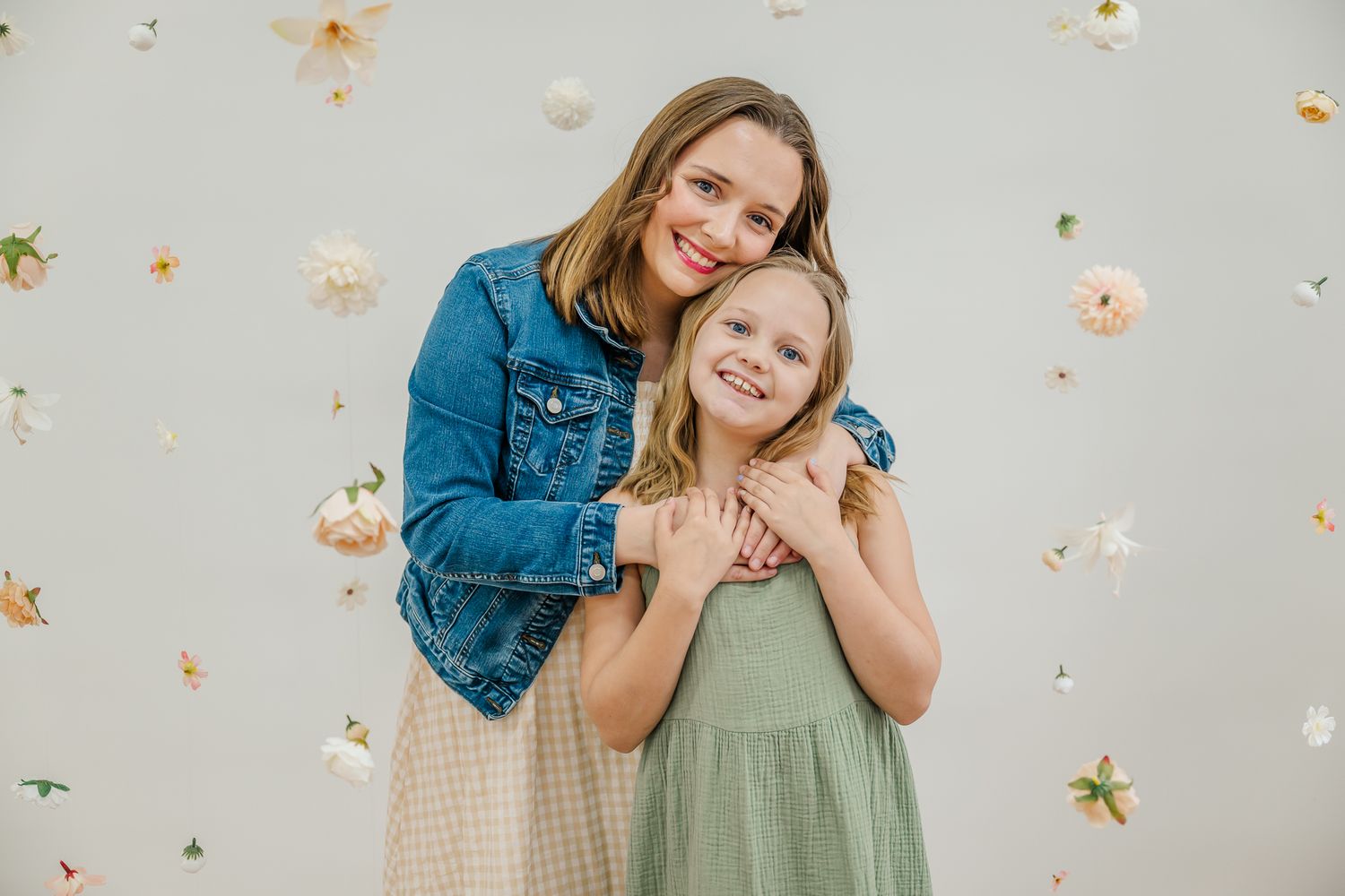 Two people in casual outfits pose together against a light background with soft floral decorations.