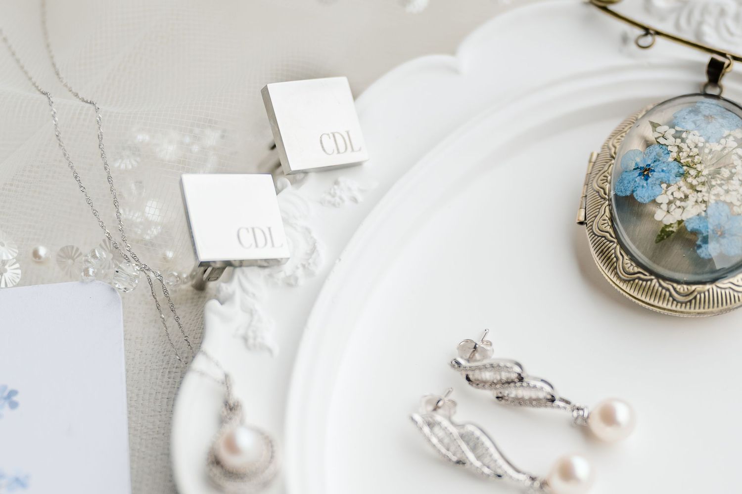 Elegant white and gold wedding invitation suite with delicate floral details and decorative accessories arranged on marble.