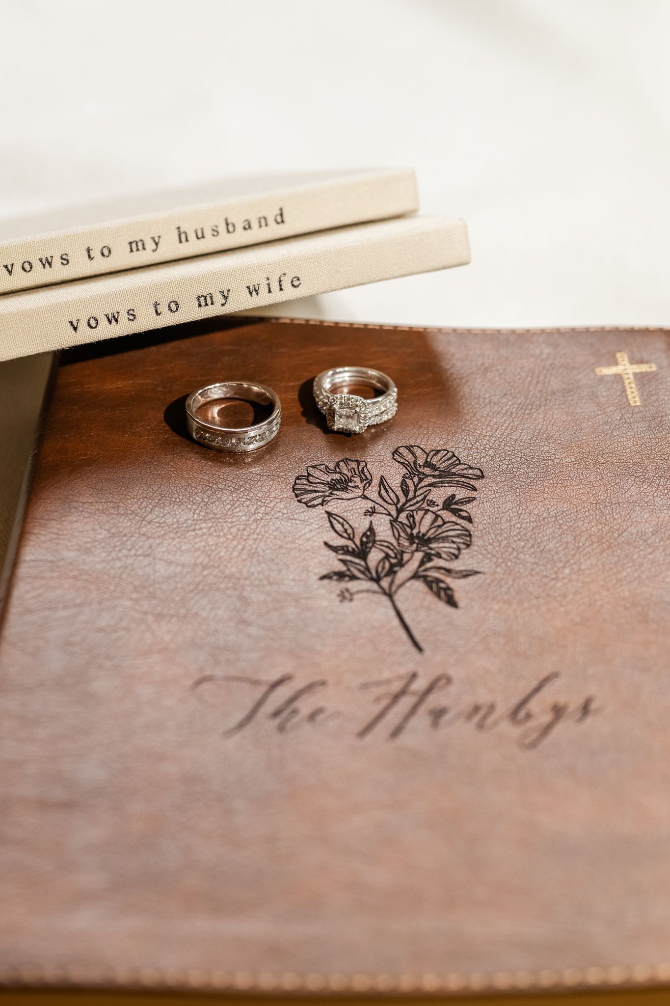 Wedding rings rest on a leather-bound vow book engraved, alongside vows to my husband and wife booklets.
