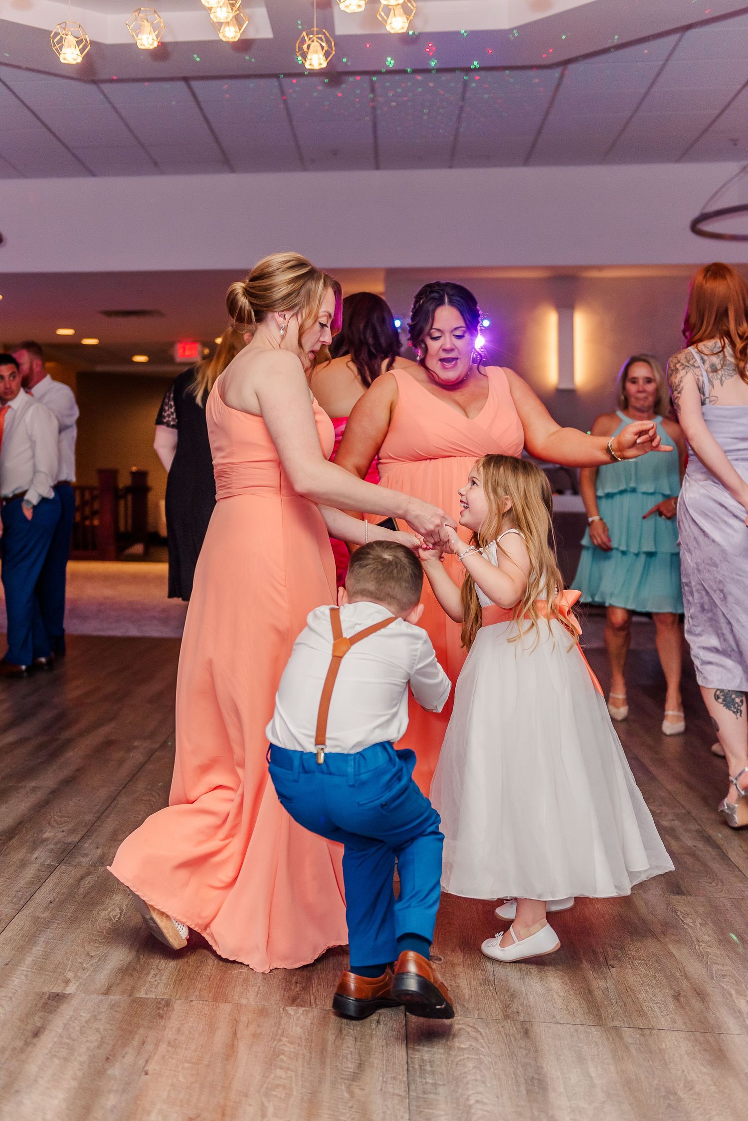 Wedding reception dance floor with guests in coral bridesmaid dresses and formal attire dancing together.