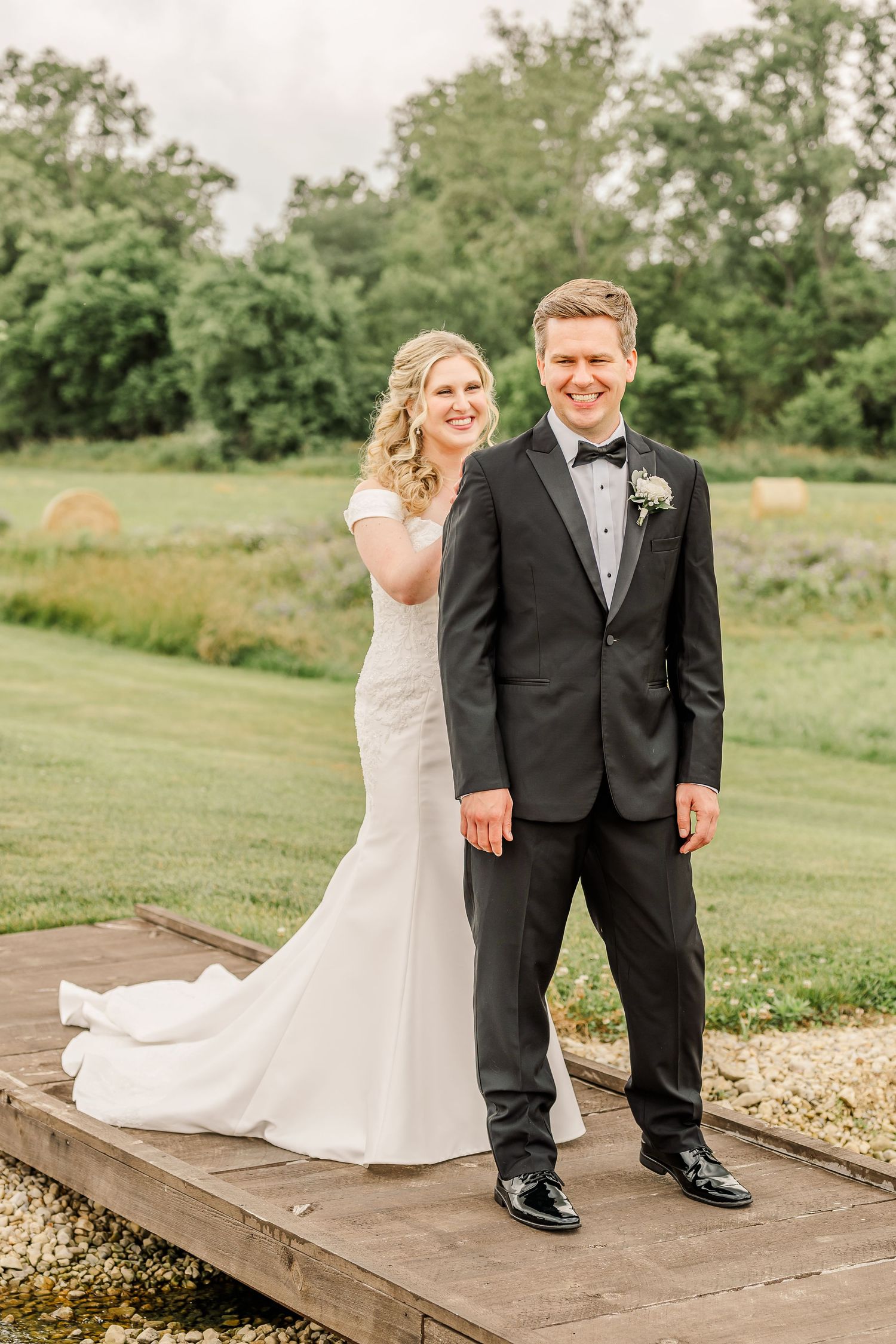 A couple poses on wooden deck surrounded by lush greenery during outdoor wedding photoshoot.The Old Barns at Dry Run Farms in Williamsport,