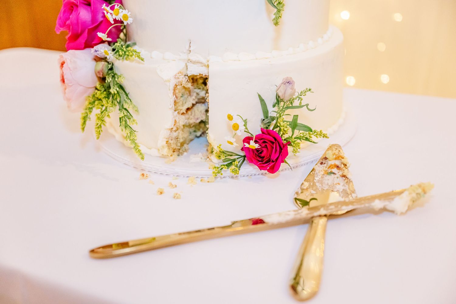Bright pink flowers and delicate greenery arranged with gold accents on a white surface create an elegant table setting.