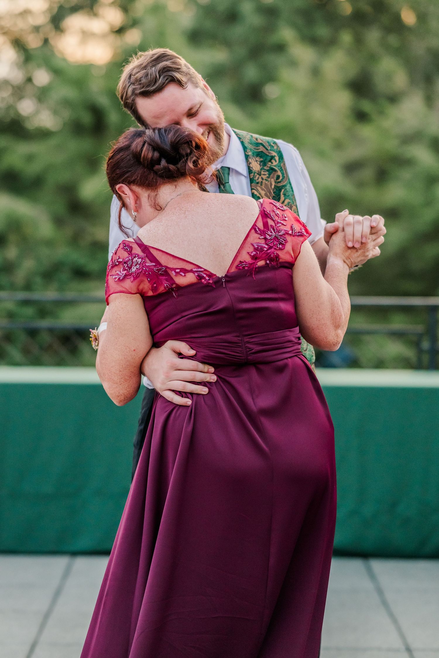 A couple in formal attire share an intimate dance moment, with the person in burgundy dress being dipped gracefully.