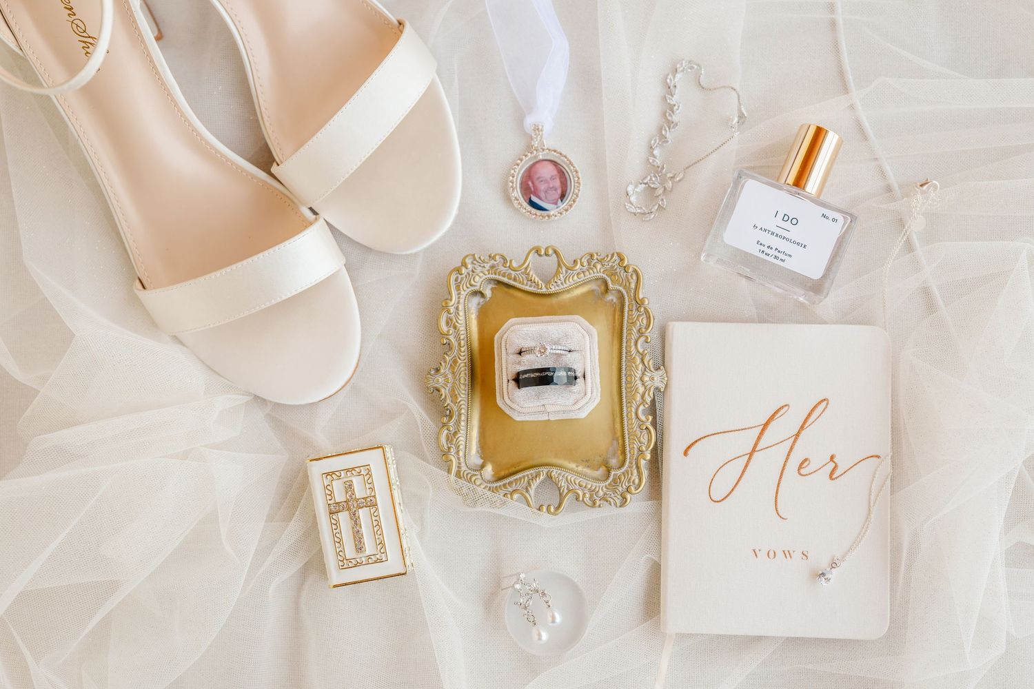Elegant wedding accessories including white ribbons, invitations, and perfume bottles arranged on light beige surface.