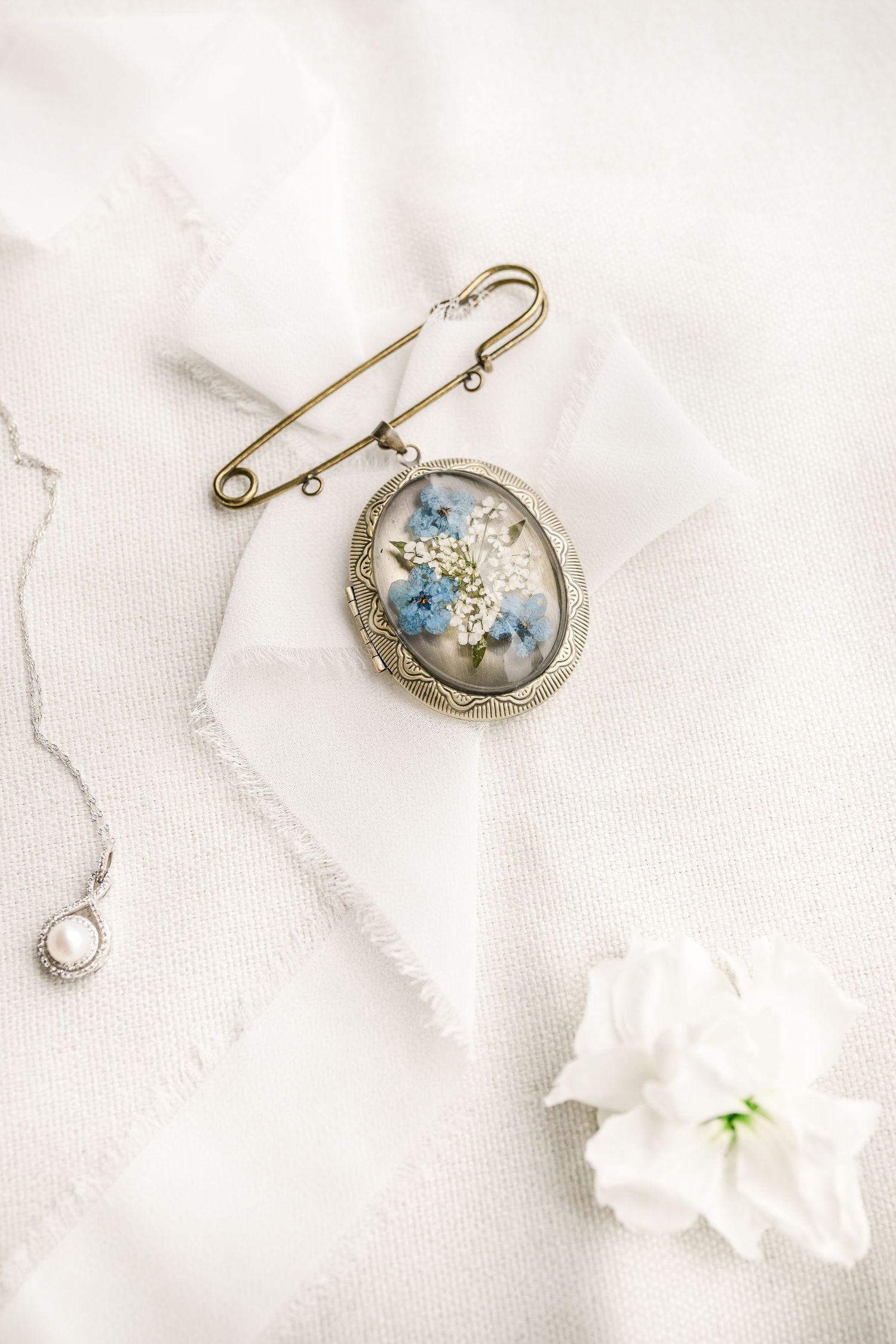 Vintage oval locket brooch with blue floral design on white fabric next to a delicate white flower.