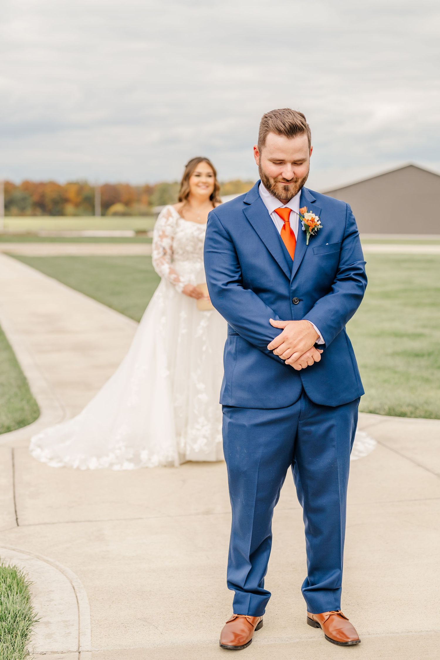 A wedding couple poses playfully on a concrete path with autumn foliage in the background.