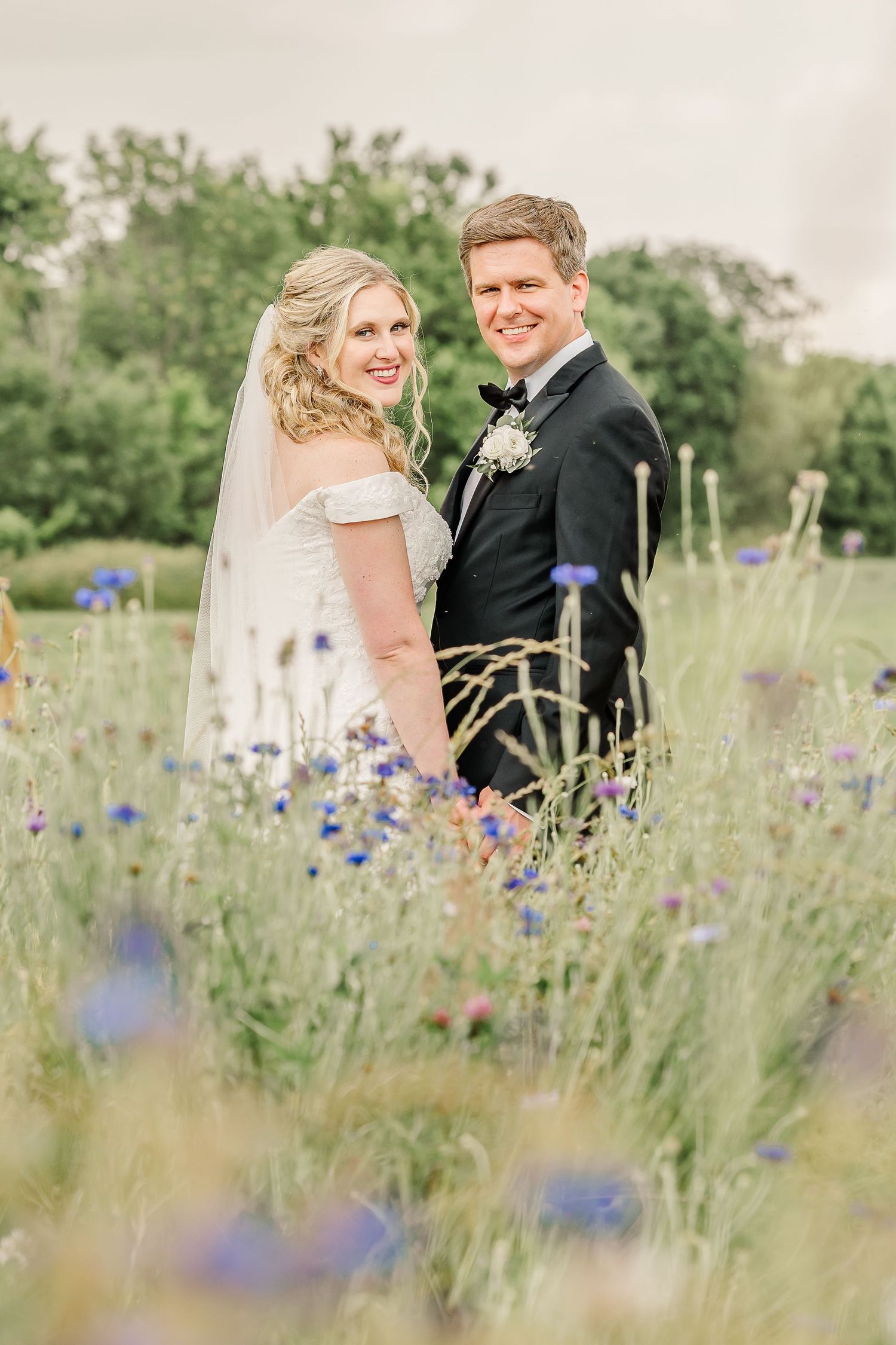 A newlywed couple poses in a wildflower meadow with purple blooms on a summer day.The Old Barns at Dry Run Farms in Williamsport, OH.