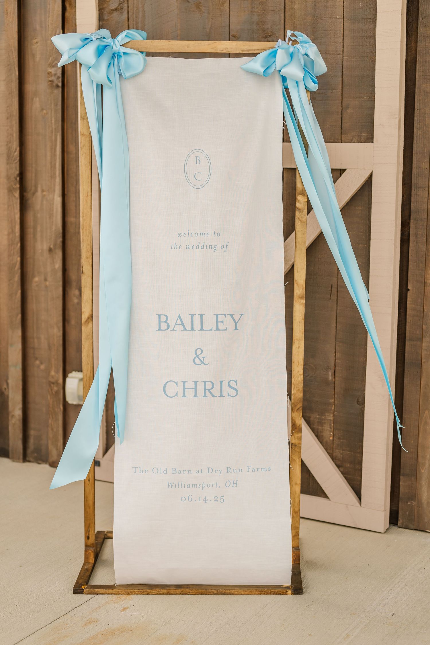 Wedding signs with names Bailey and Chris hang from light blue ribbons against a rustic wooden wall.The Old Barns at Dry Run Farms