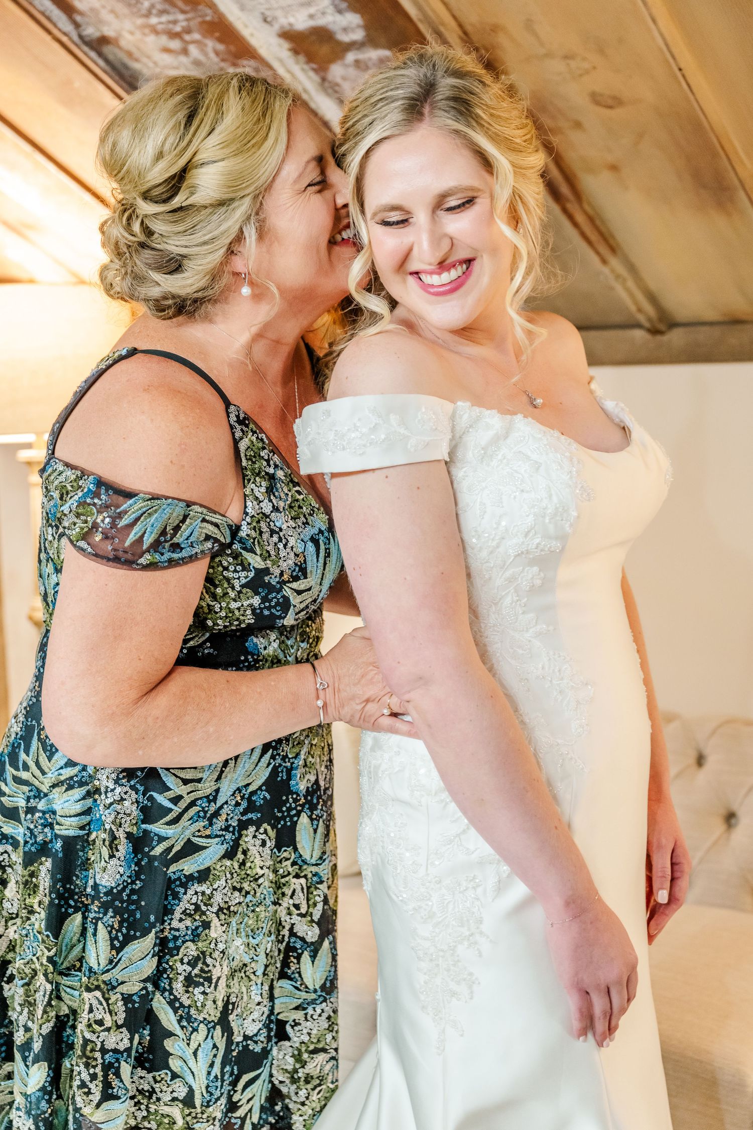 Two figures embrace in an emotional moment, one wearing a floral dress and one in a white wedding gown. The Old Barns at Dry Run Farms