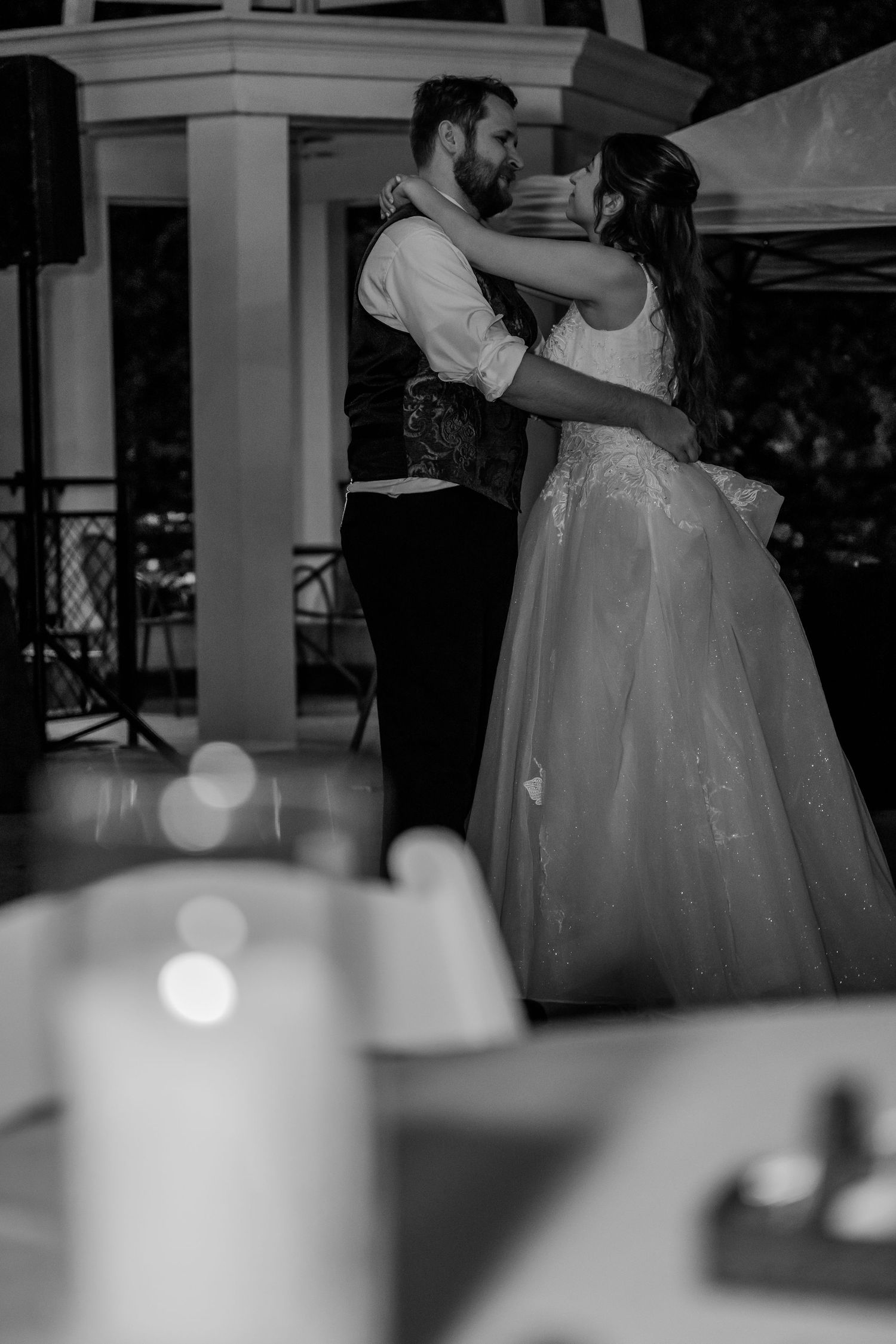 Black and white image of couples dancing at an evening reception with candlelit tables.