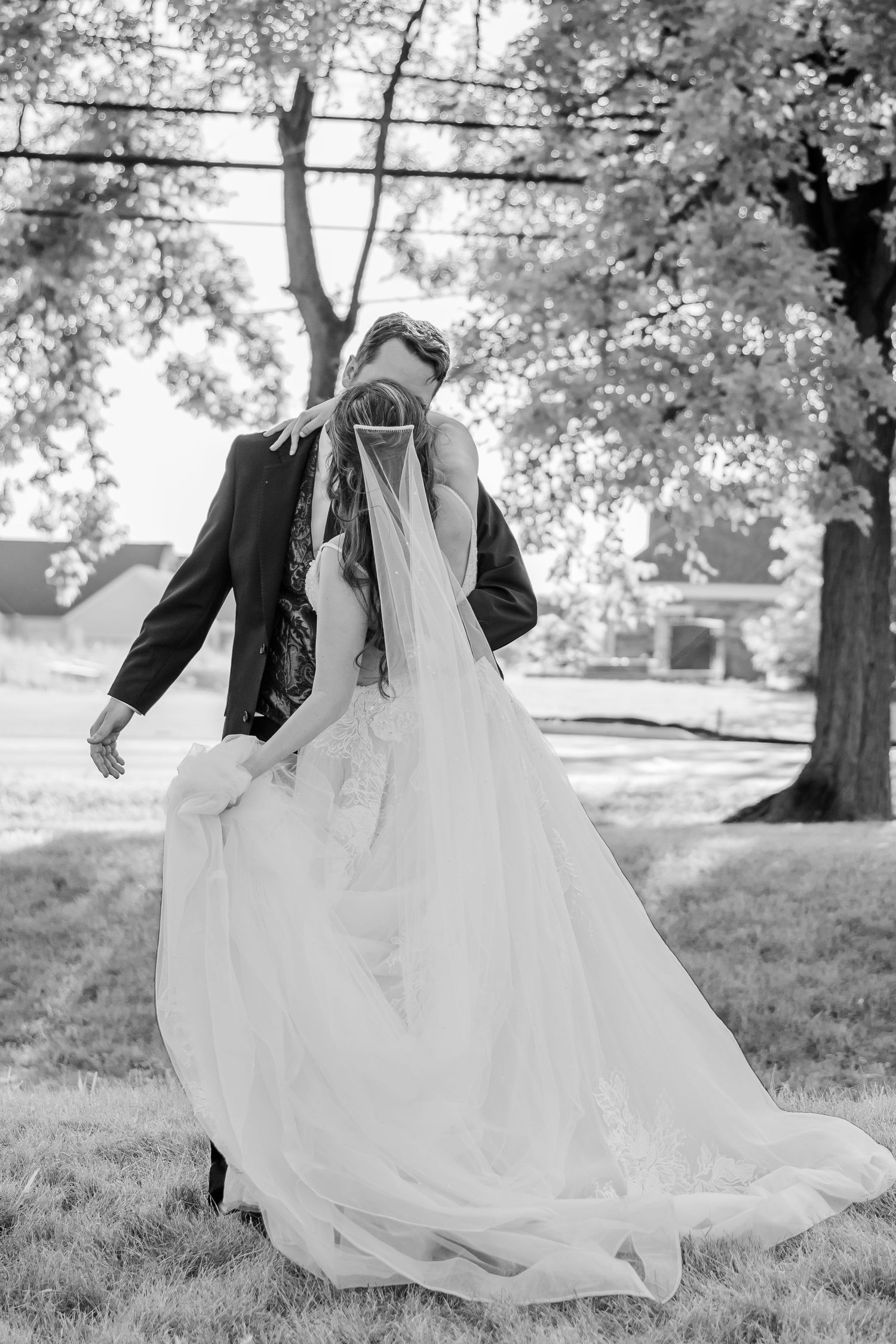 Black and white photo of flowing wedding dress train on grassy lawn.
