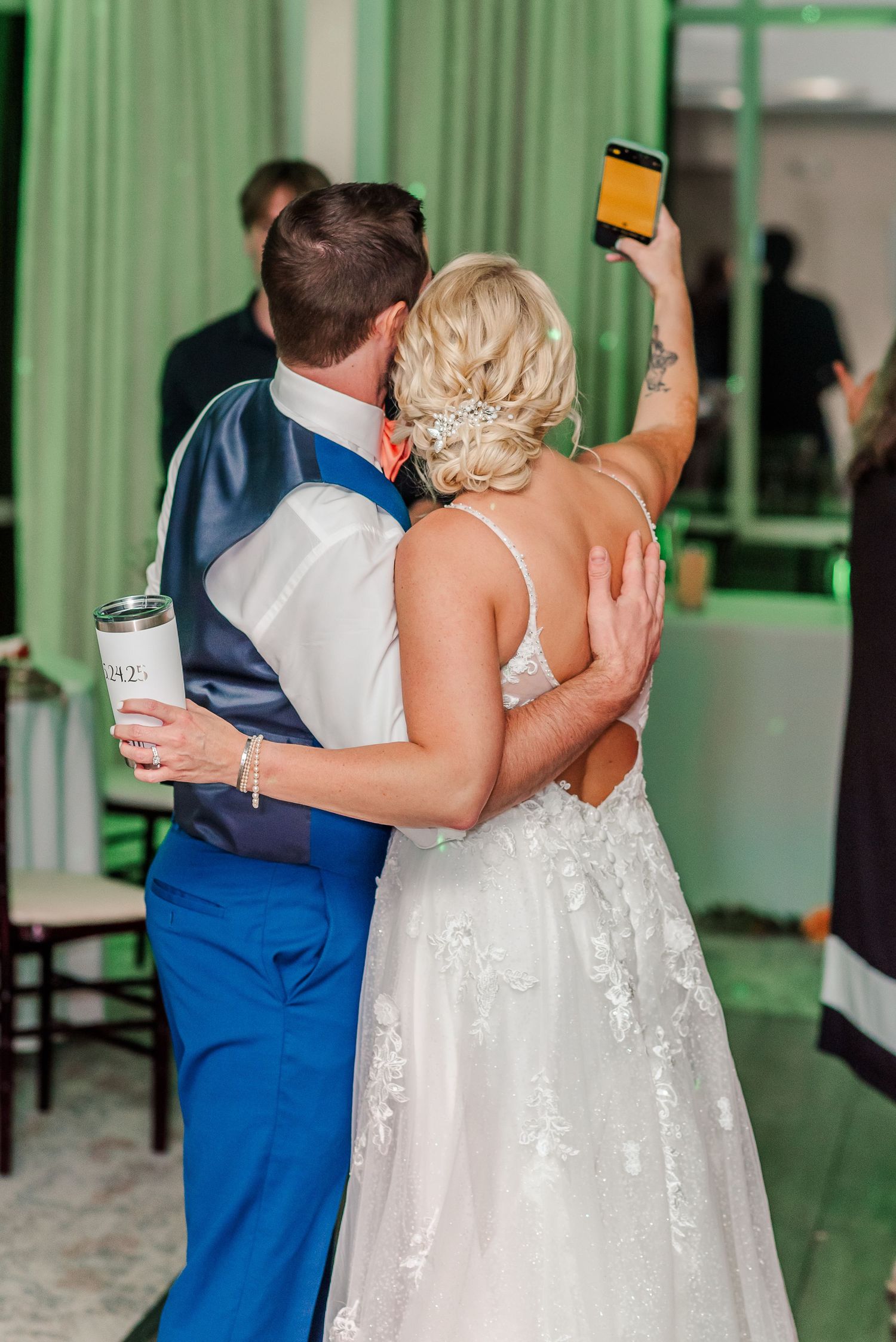 Wedding guests dancing in a reception venue with green-tinted lighting and white curtains.