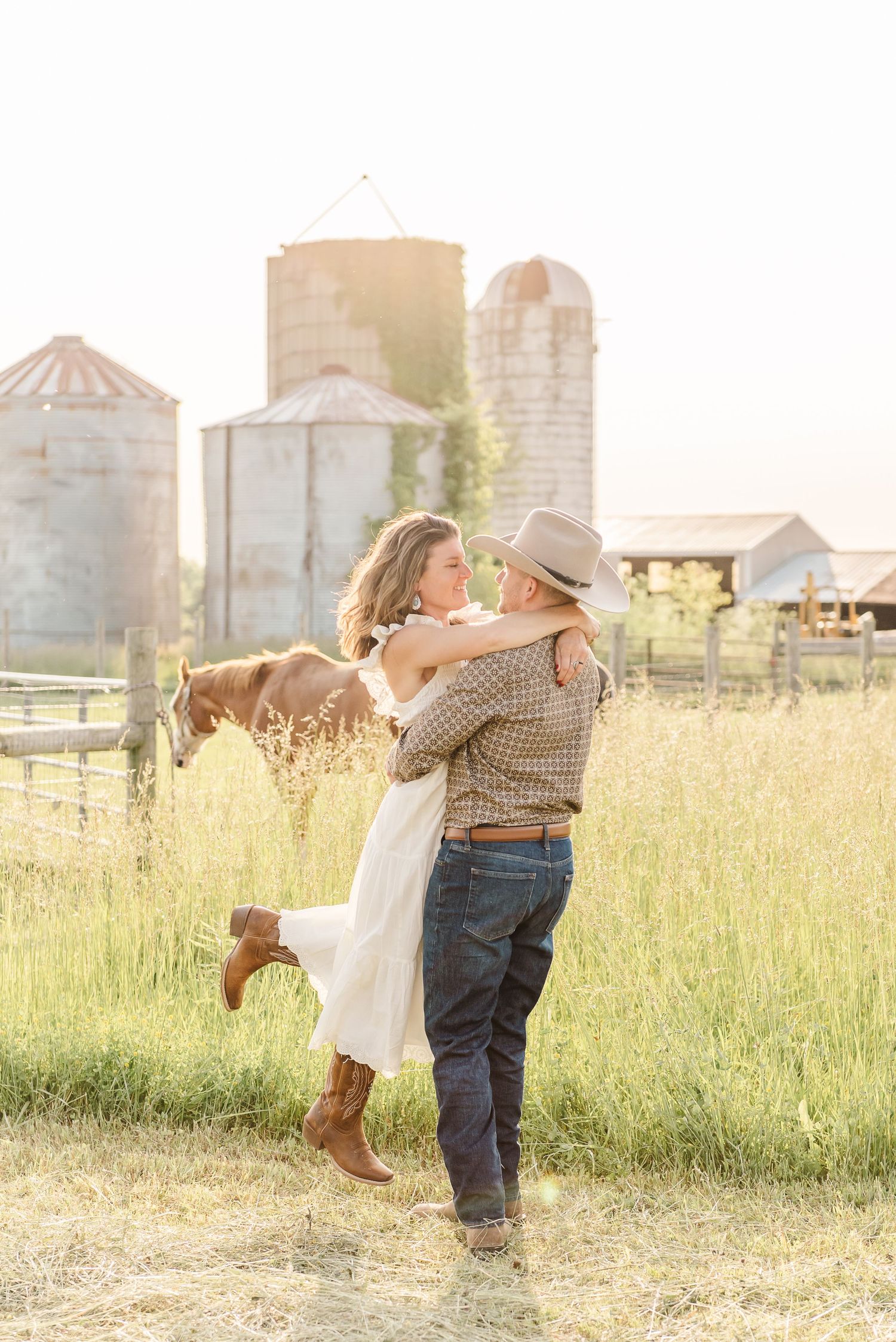 A romantic couple dances together in a sunlit field with farm silos visible in the background.