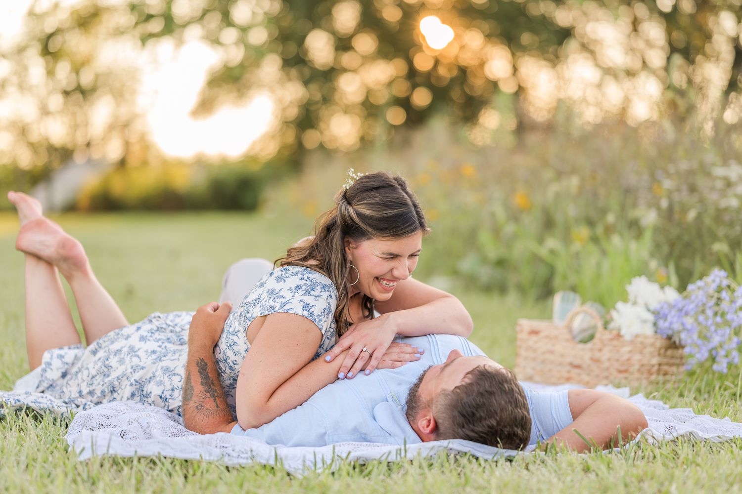Couple sharing a romantic moment on a blanket in a sunny meadow during a golden hour outdoor picnic photoshoot.