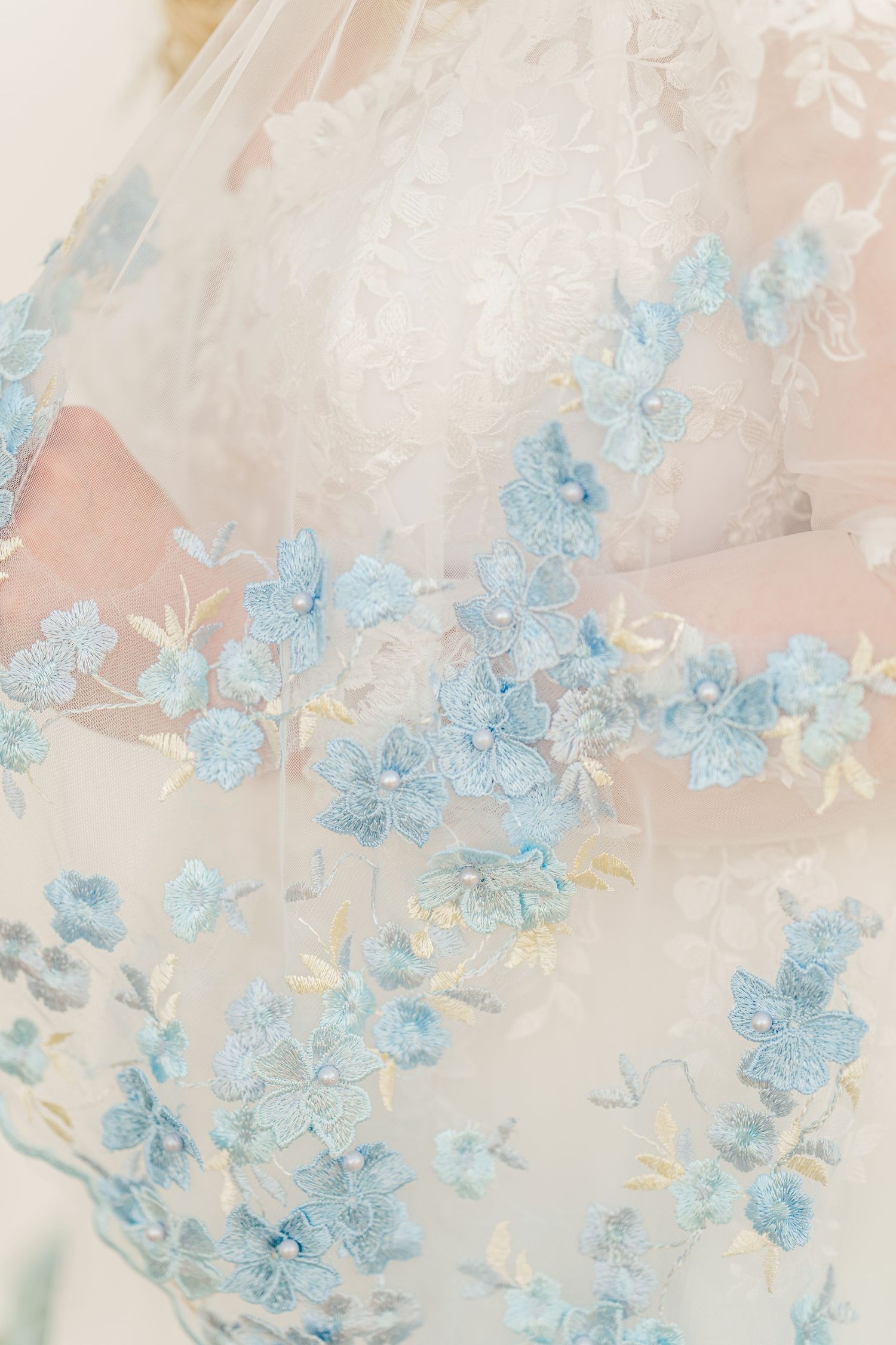 Delicate blue floral pattern overlay on soft white fabric with ethereal lighting and dreamy texture.