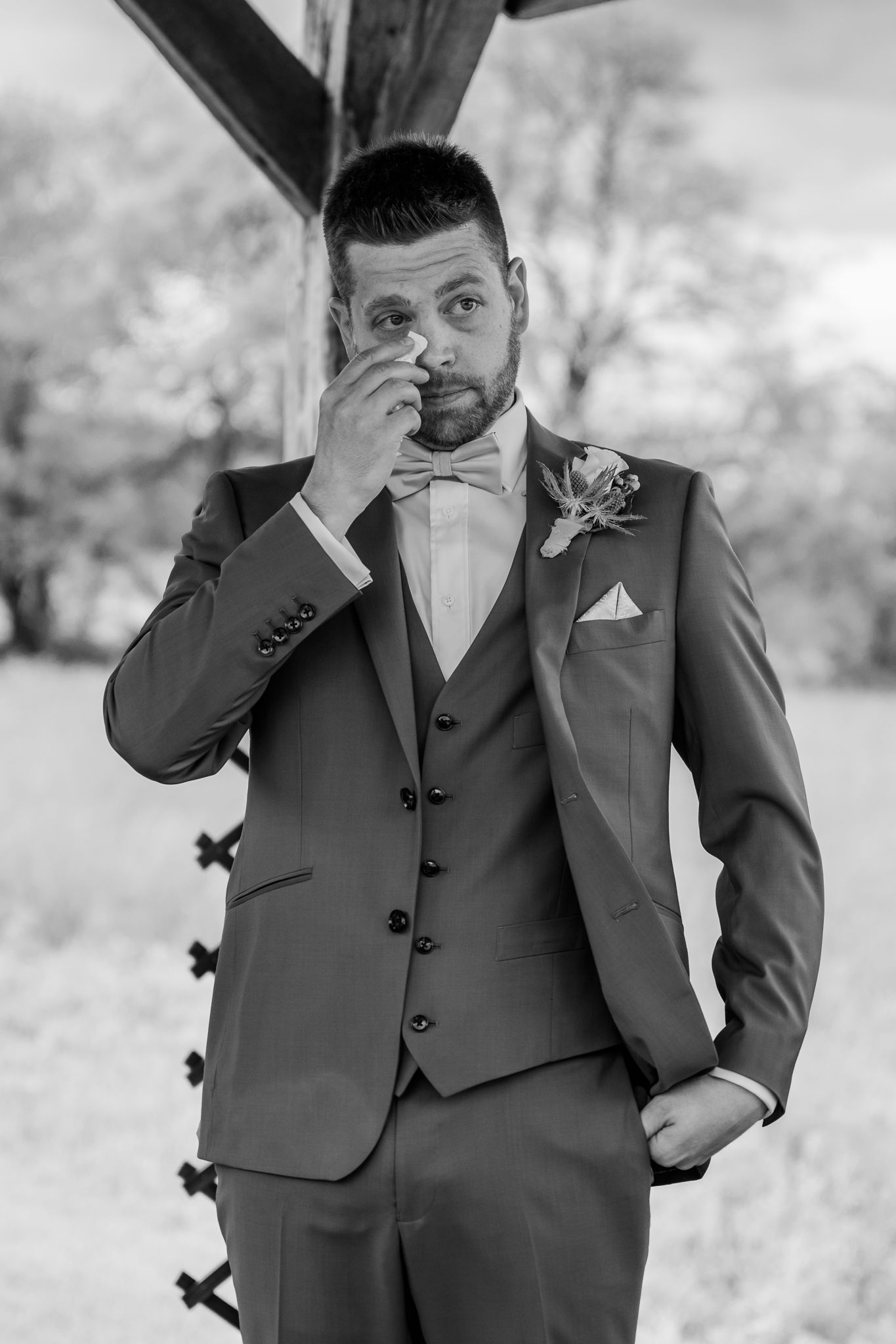 Emotional groom in gray three-piece suit with bow tie wiping tear at outdoor wedding ceremonyThe Old Barns at Dry Run Farms in Williamsport.