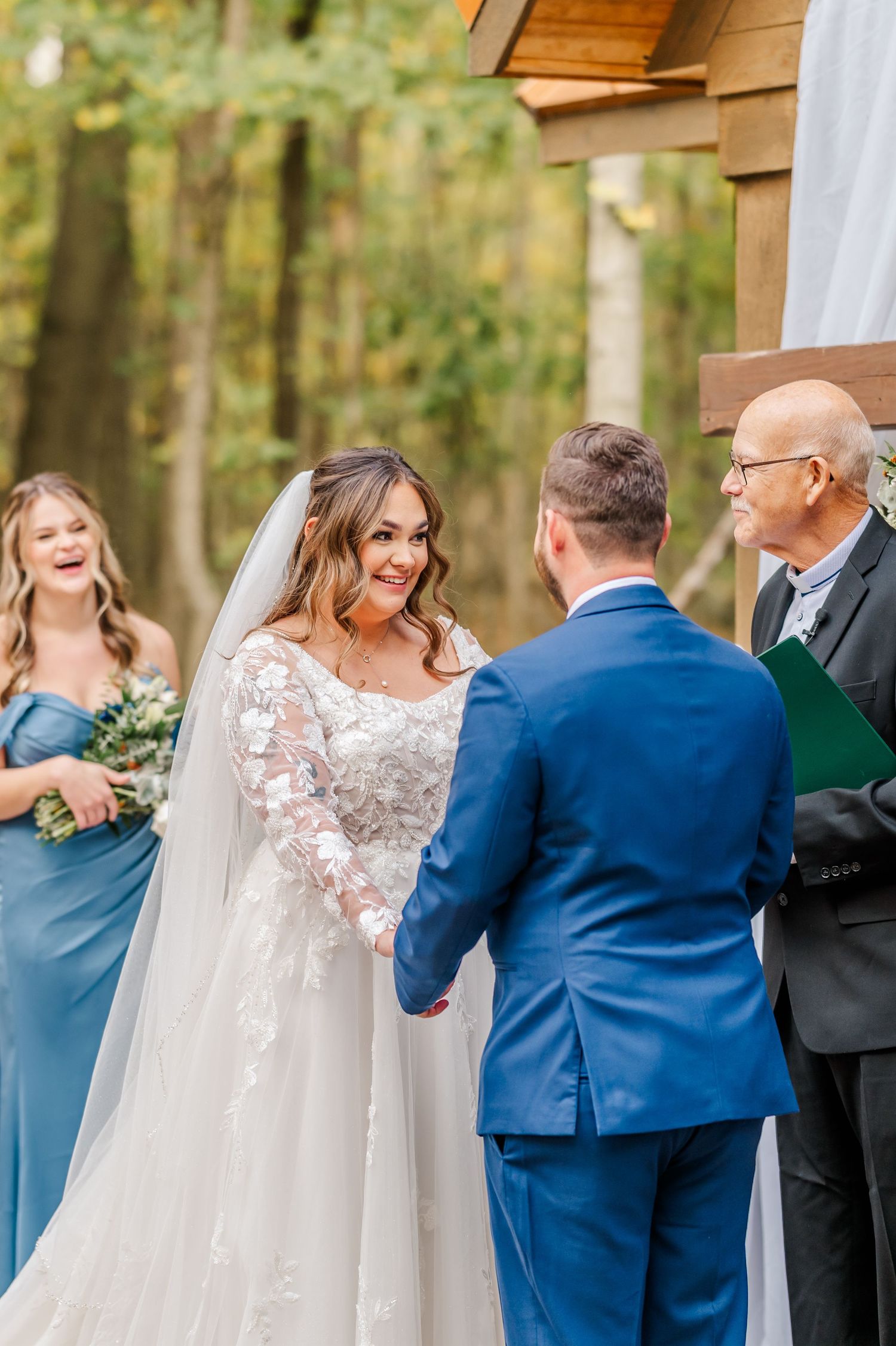 Wedding ceremony taking place outdoors with attendants wearing blue and white attire.Four Seasons Barn Wedding & Event Venue