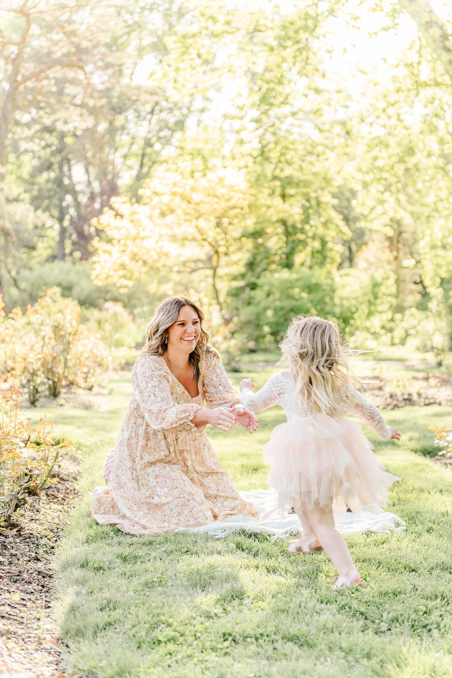 Mother and daughter in flowing dresses playing together on grassy hill during sunset photoshoot.