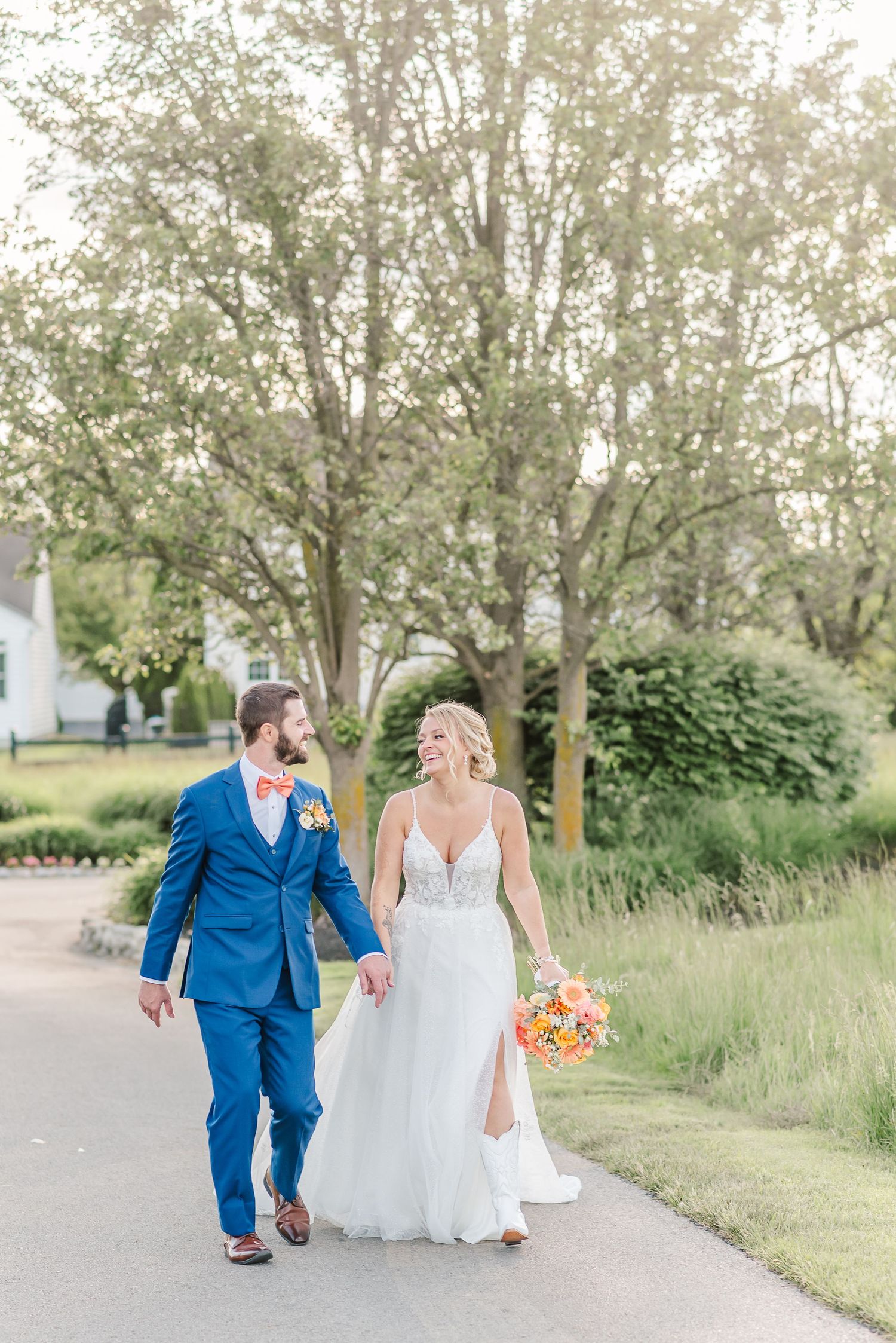 A couple walking together on a garden path, with the person in a blue suit and white dress holding bright bouquet.